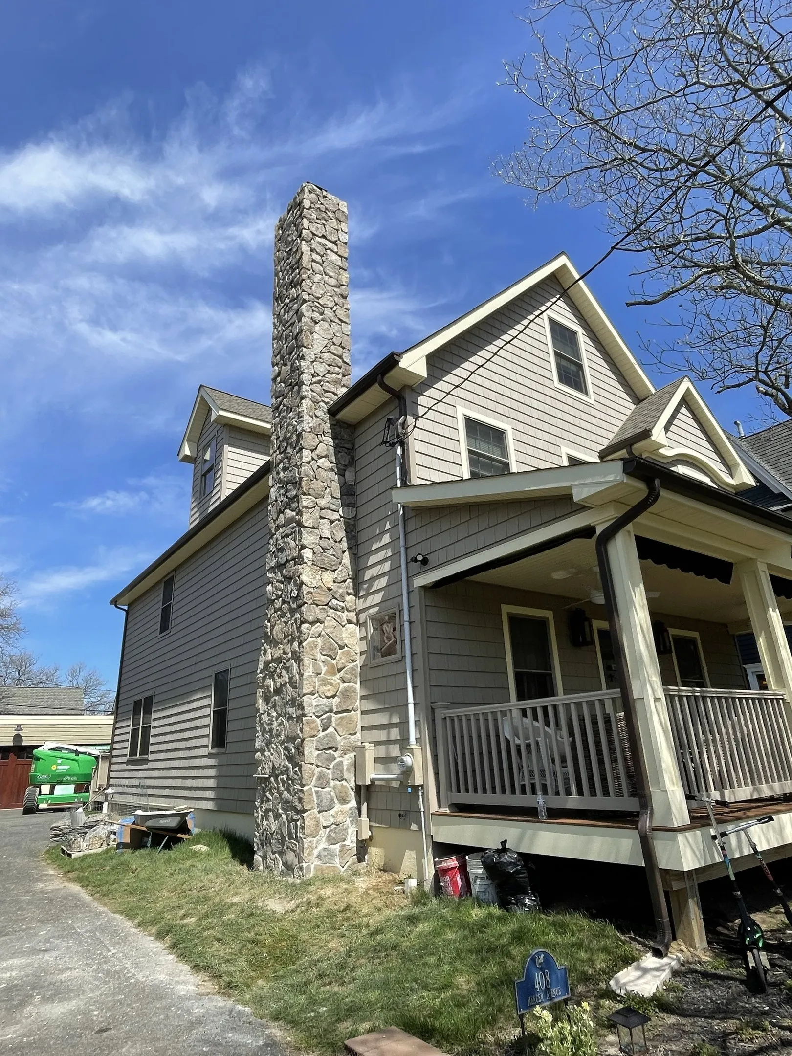 A wider finished view of the stone-clad chimney beside the house siding, porch and driveway.