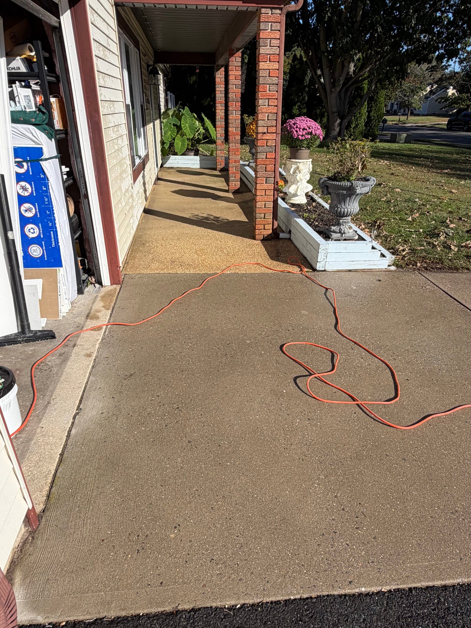 Before: the concrete surface beside the garage and covered entry, with a cleaning hose across it.