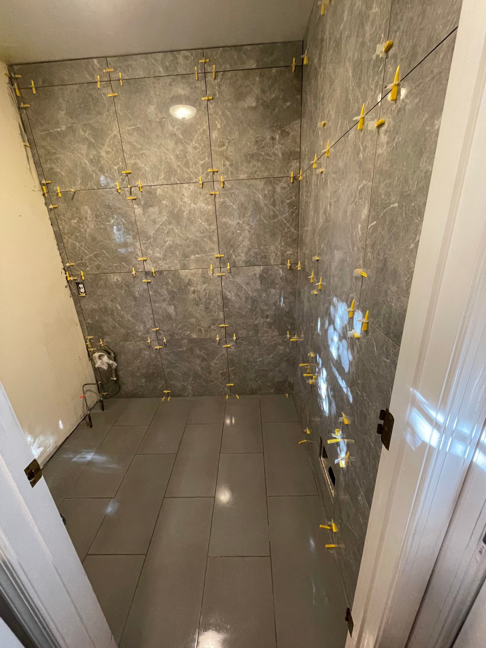 Gray marble-look wall tile and floor tile during installation, with leveling clips in place.