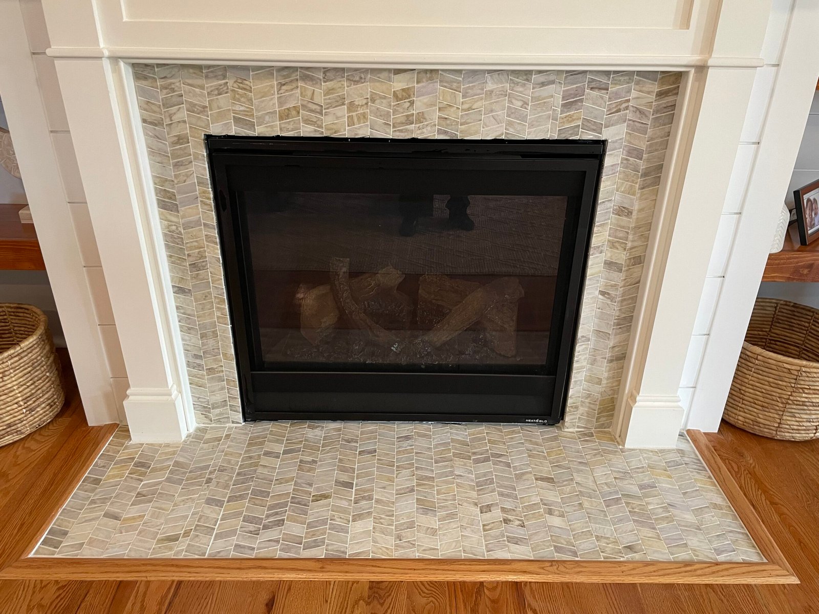 After: chevron mosaic around the fireplace opening and across the hearth, framed by the white surround and wood floor edging.