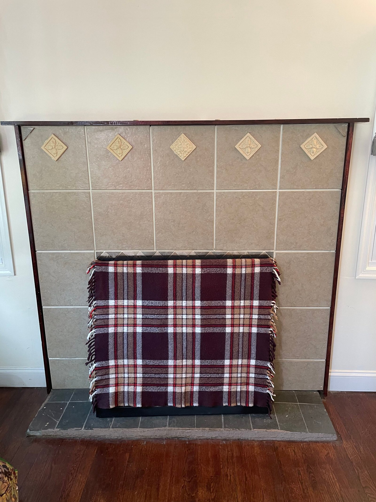 Before: a closer view of the original square-tile fireplace surround and dark tiled hearth, with the opening covered.