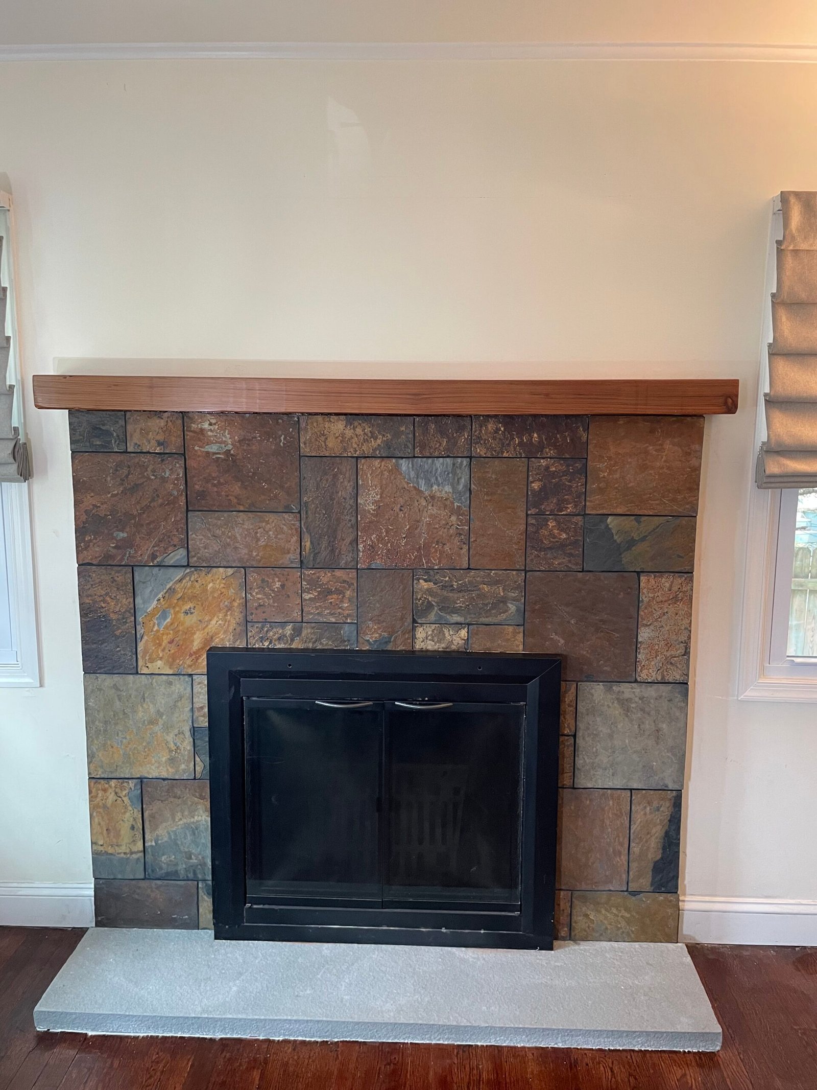 After: multitone rectangular facing, a wood mantel, a light hearth and a black-framed fireplace door assembly.