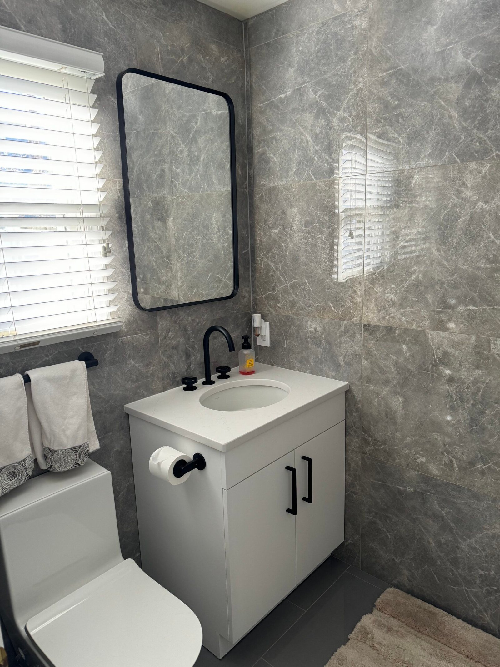 After: the white vanity, black fixtures and mirror against the finished gray wall tile.