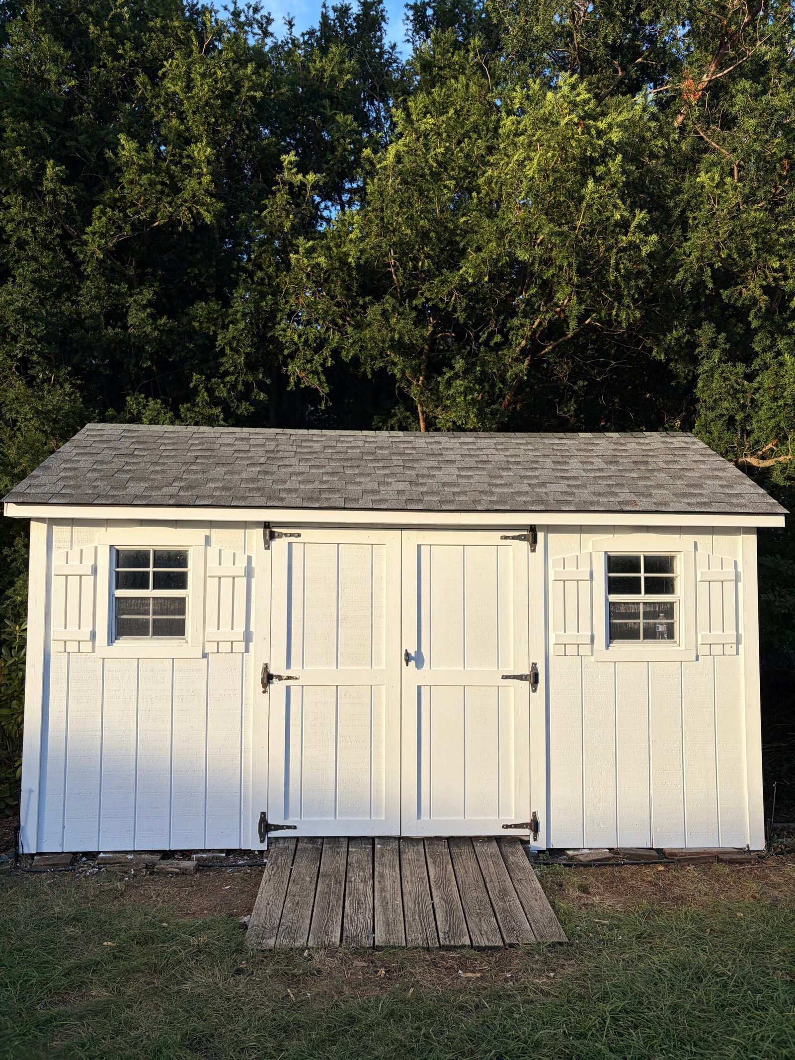 After: the renovated shed with a new shingle roof, white siding and finished double doors.