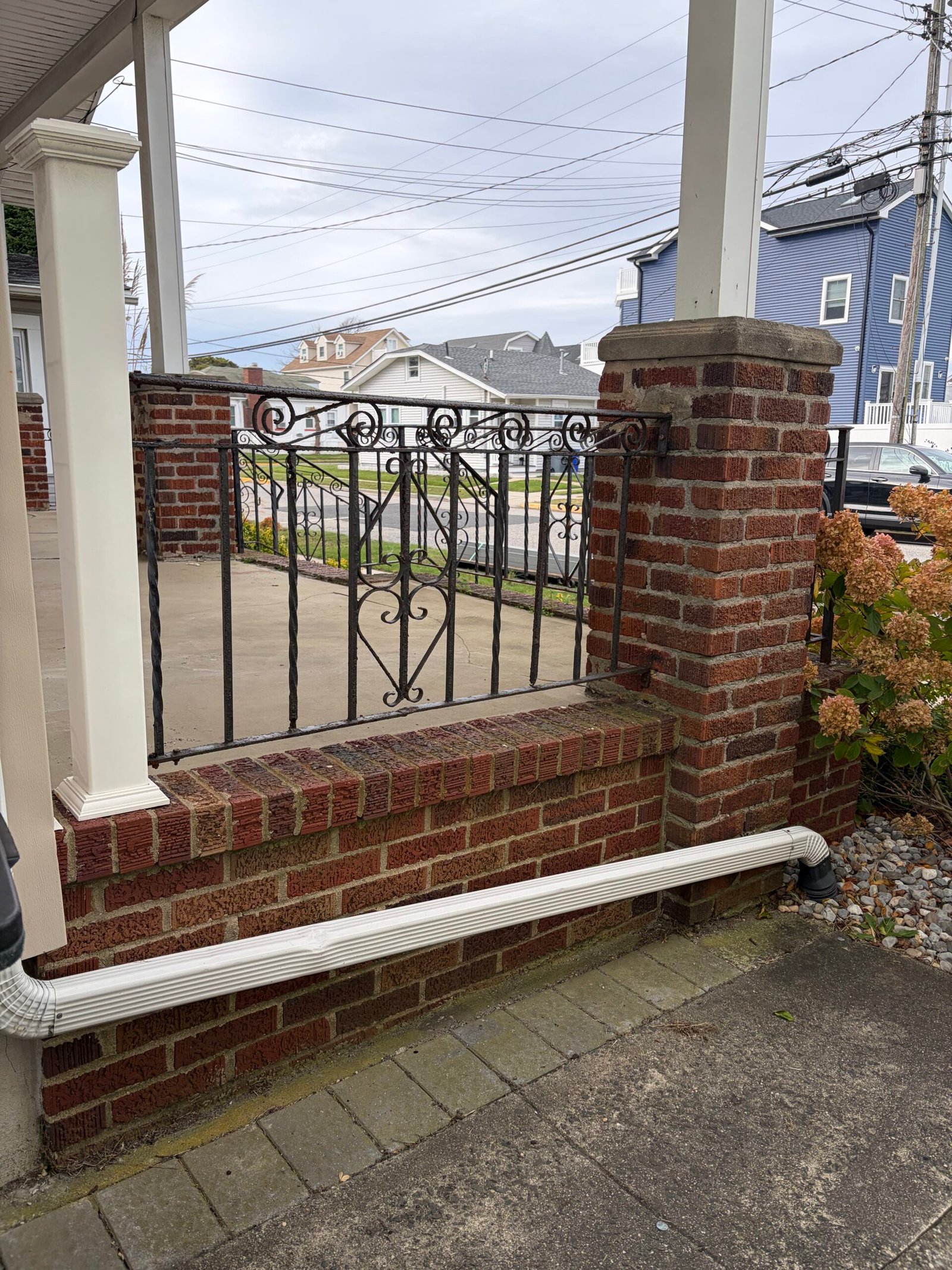 Before: the side porch wall, brick pier and retained black railing above the paved path.