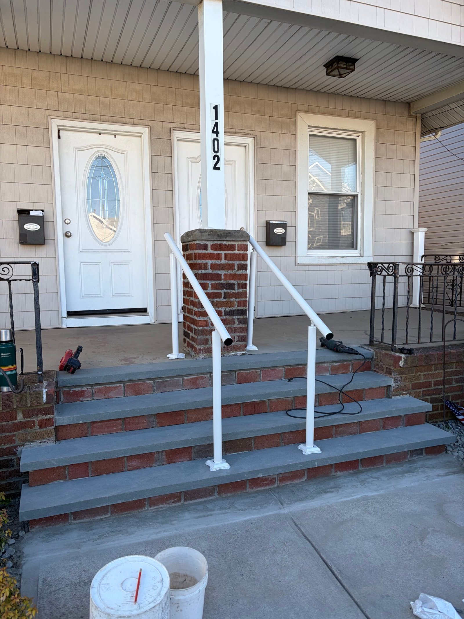 New white handrails installed beside and through the entry stairs, with the brick finish still underway.