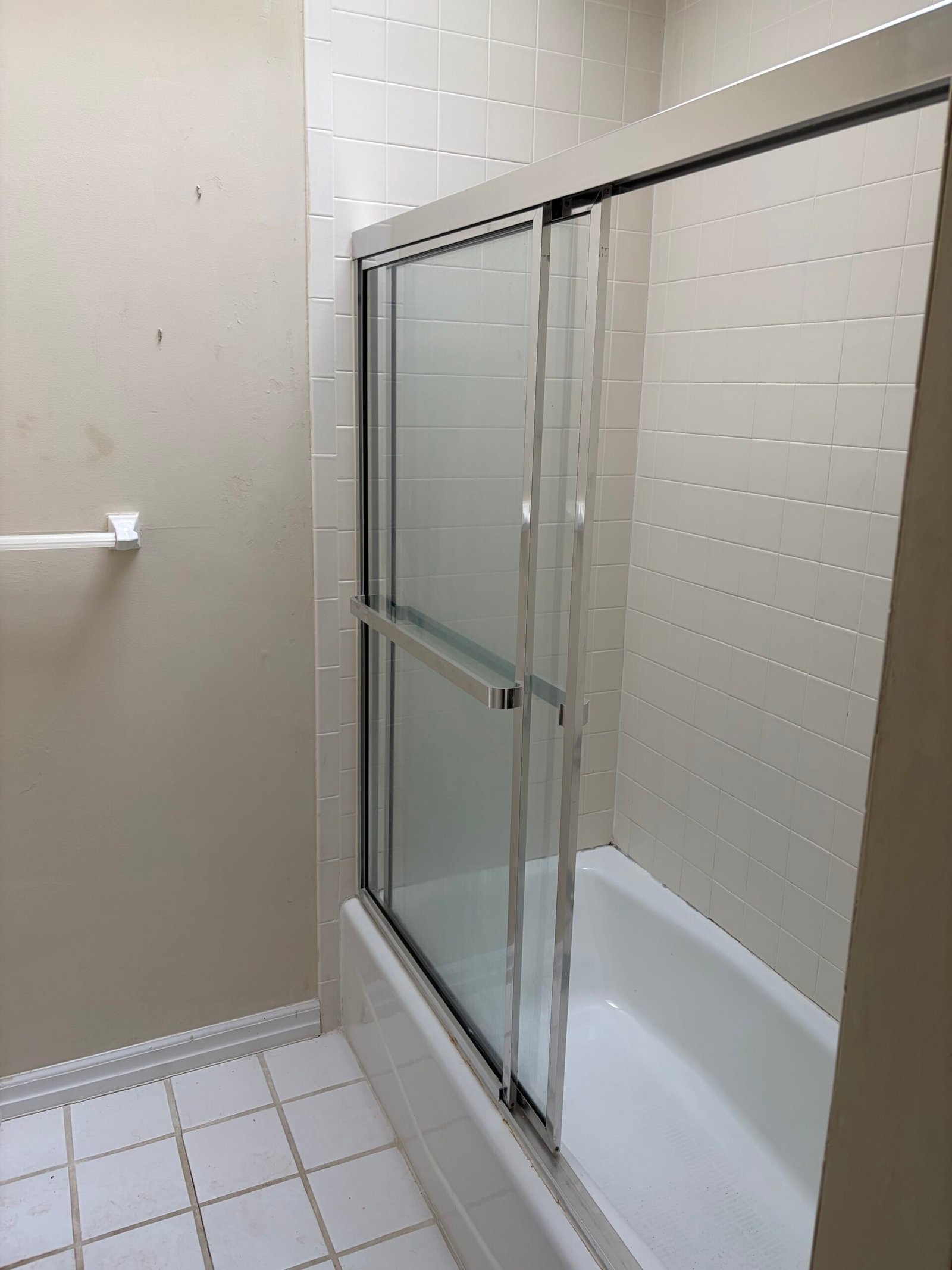 Before: the bathtub, framed glass enclosure and white tile surround.