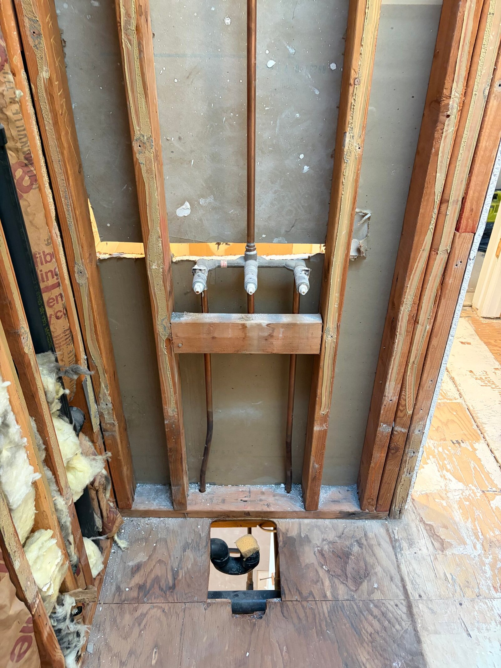 Exposed wall plumbing and the drain opening during shower preparation.