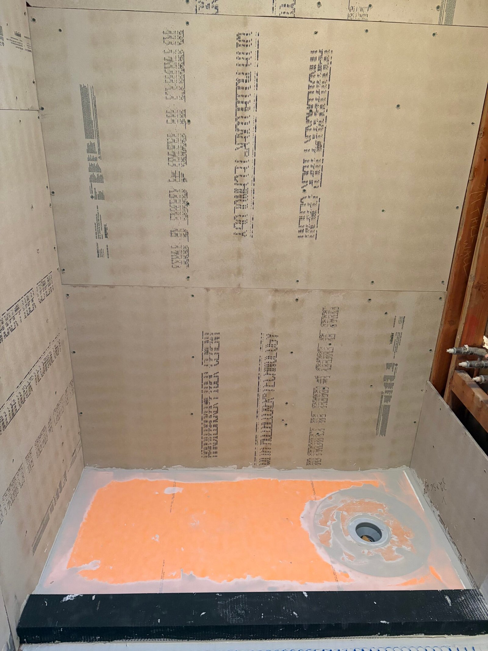 The new shower base and drain set within the boarded shower area.