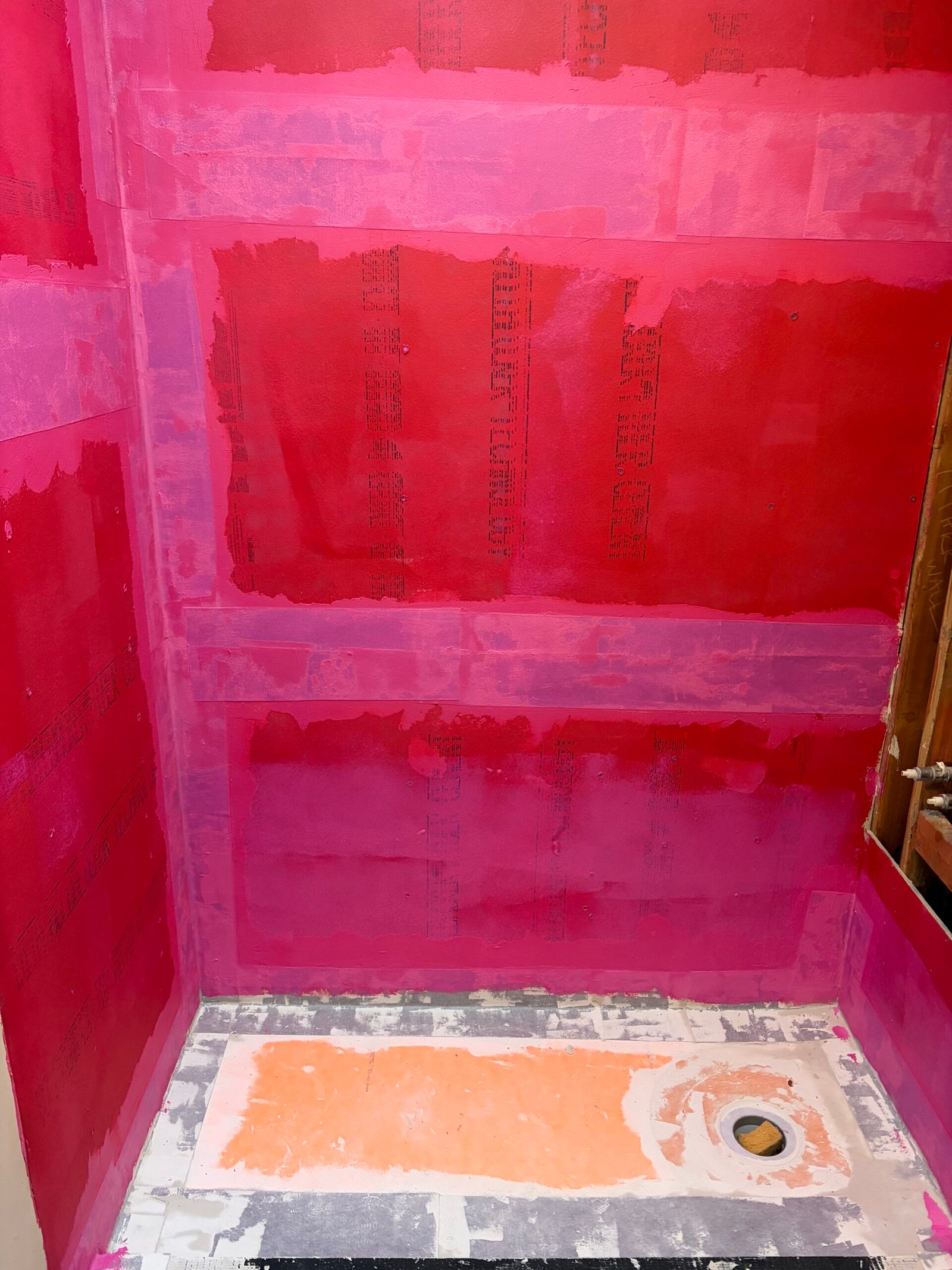 A red waterproofing coating across the prepared shower walls.