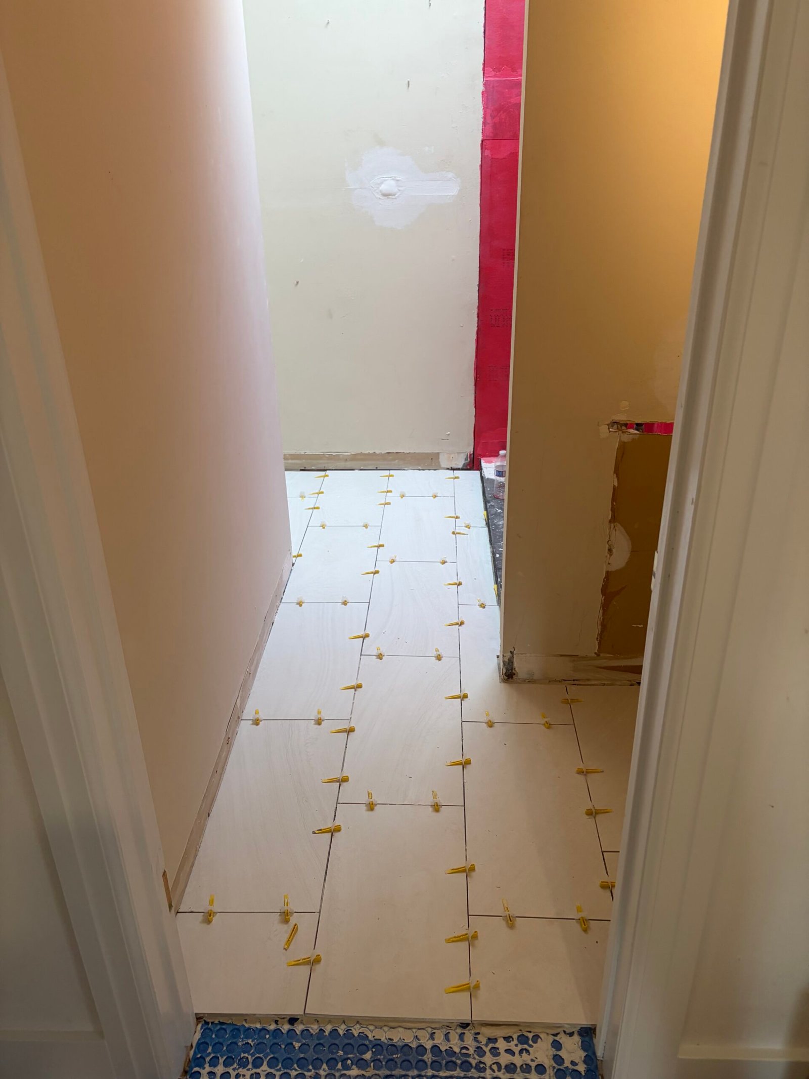 Light bathroom floor tile being installed with leveling clips in place.