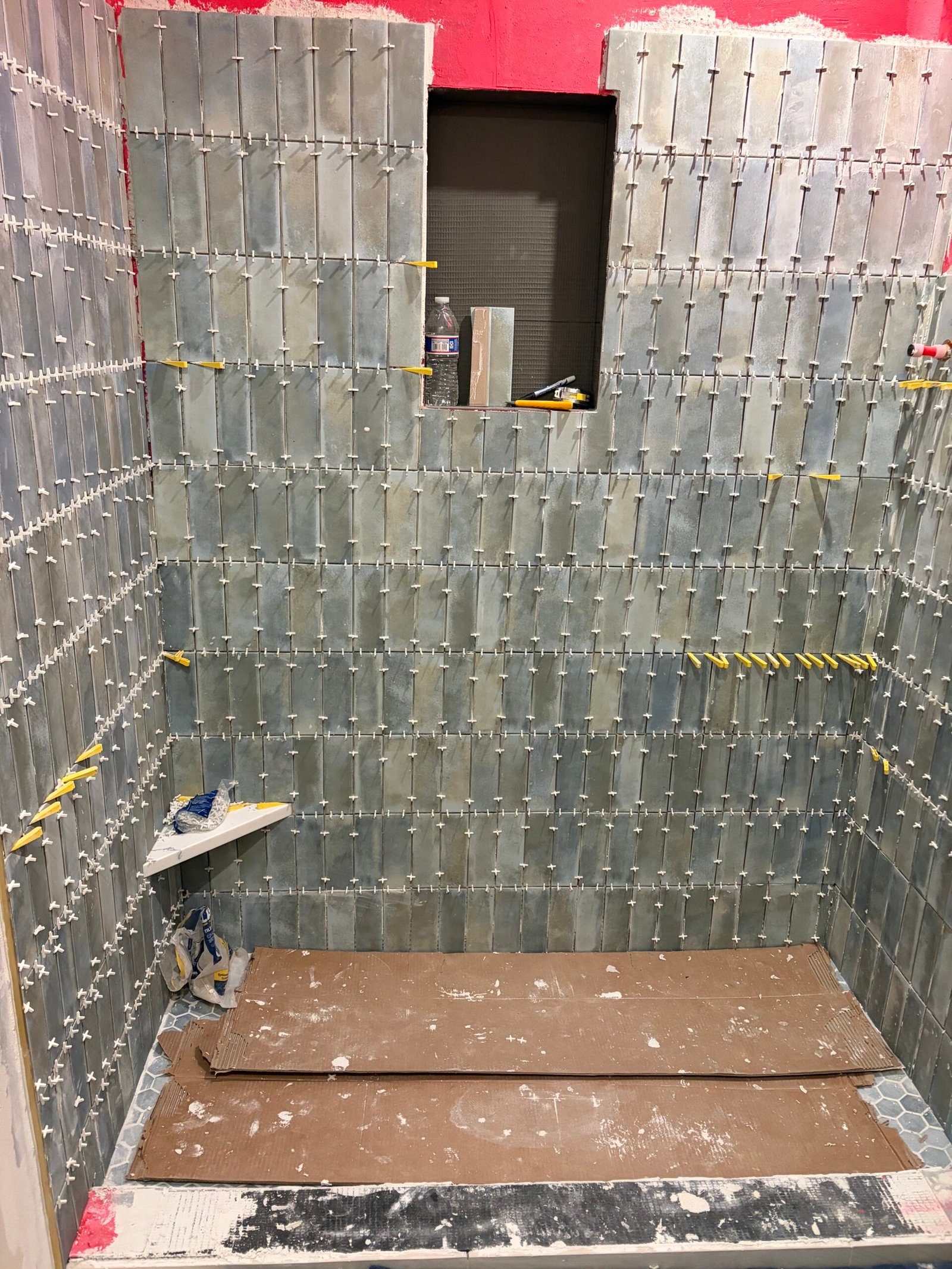 Vertical blue-gray tile being installed around the recessed shower niche.