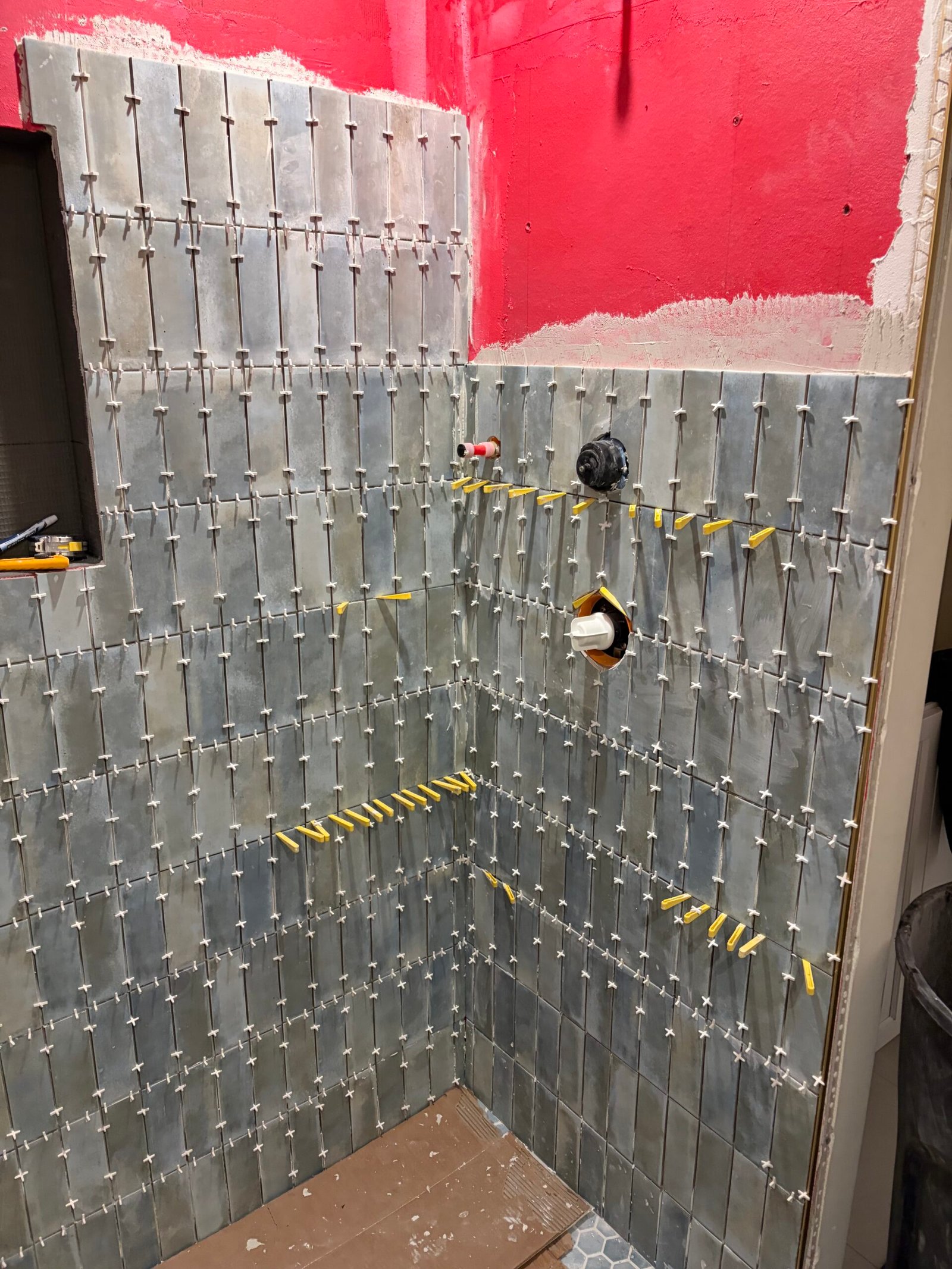 Tile progressing across the shower walls with spacers and leveling clips.