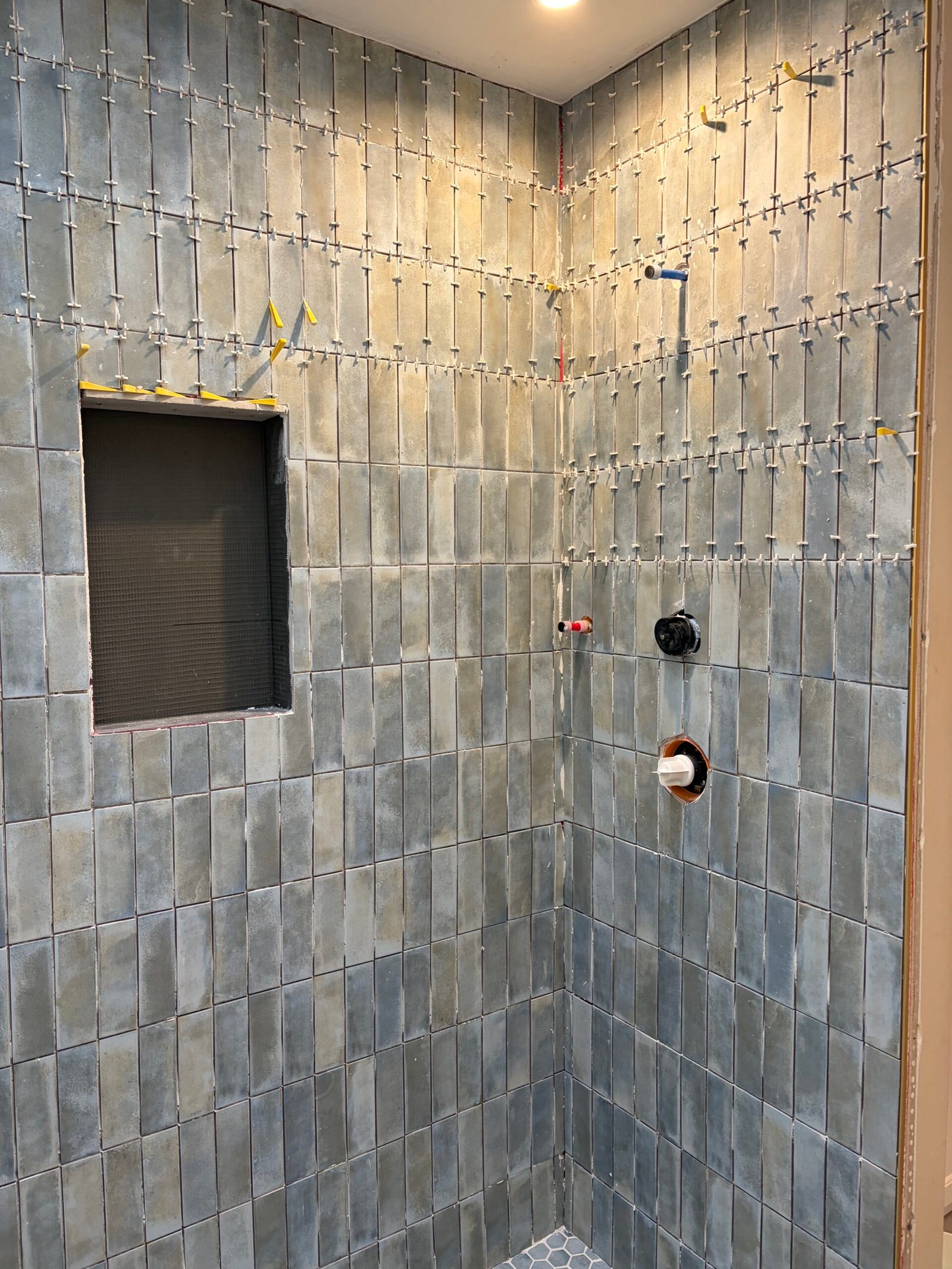 Tile set around the shower plumbing openings, with leveling clips still visible.