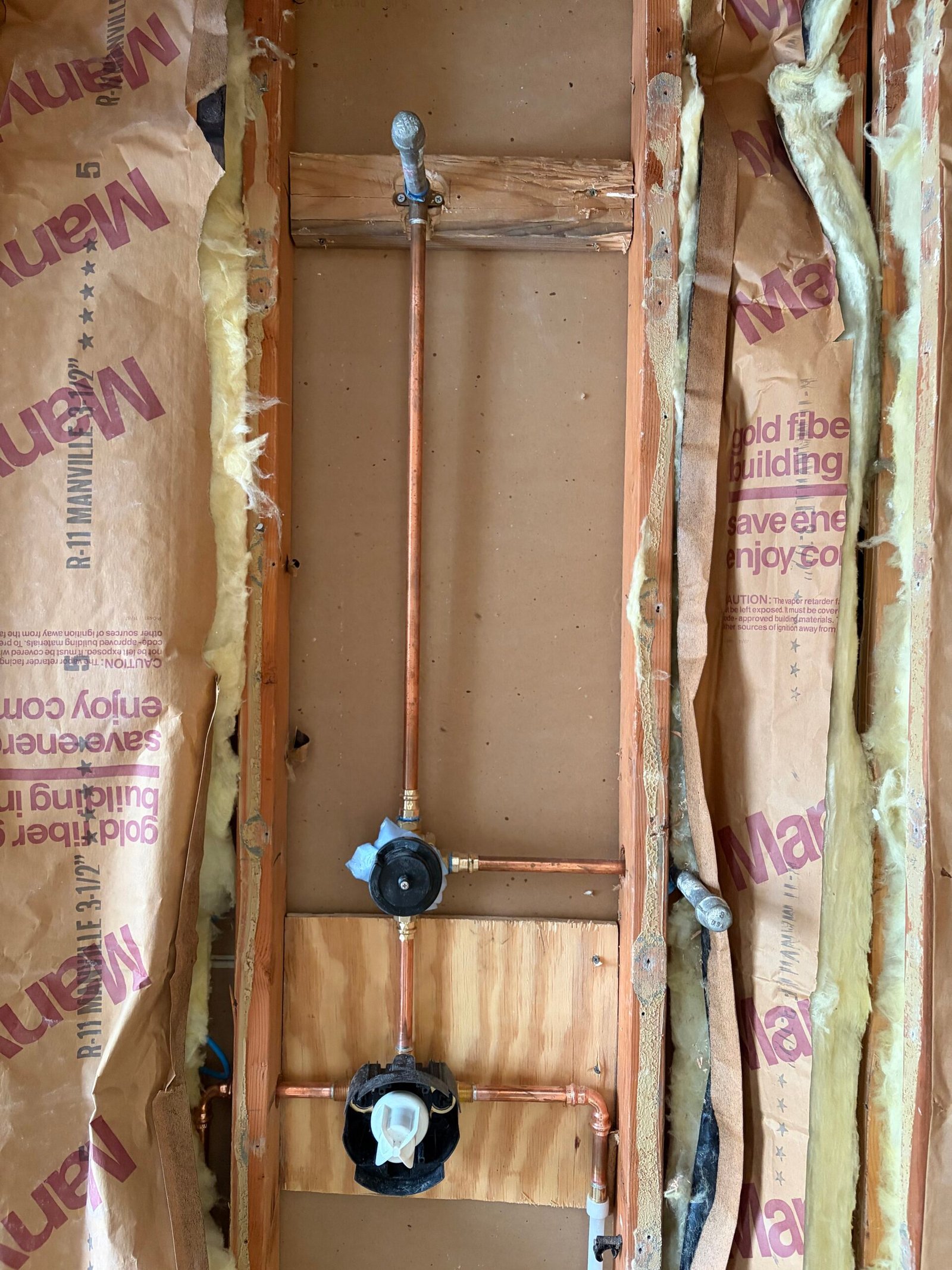 Rough shower pipework and controls visible in the open wall.