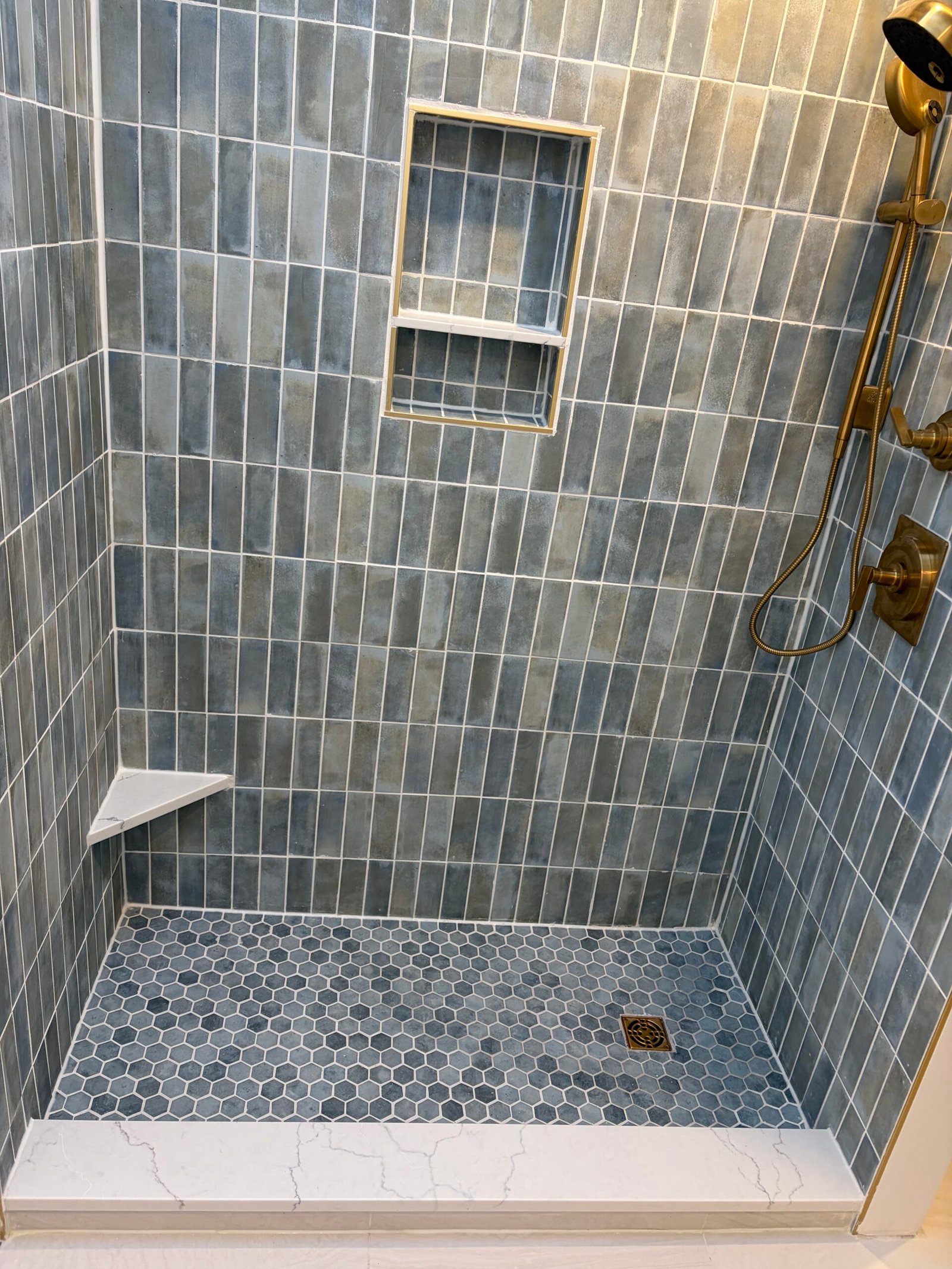 Brass-tone shower fittings above the hexagonal mosaic floor.