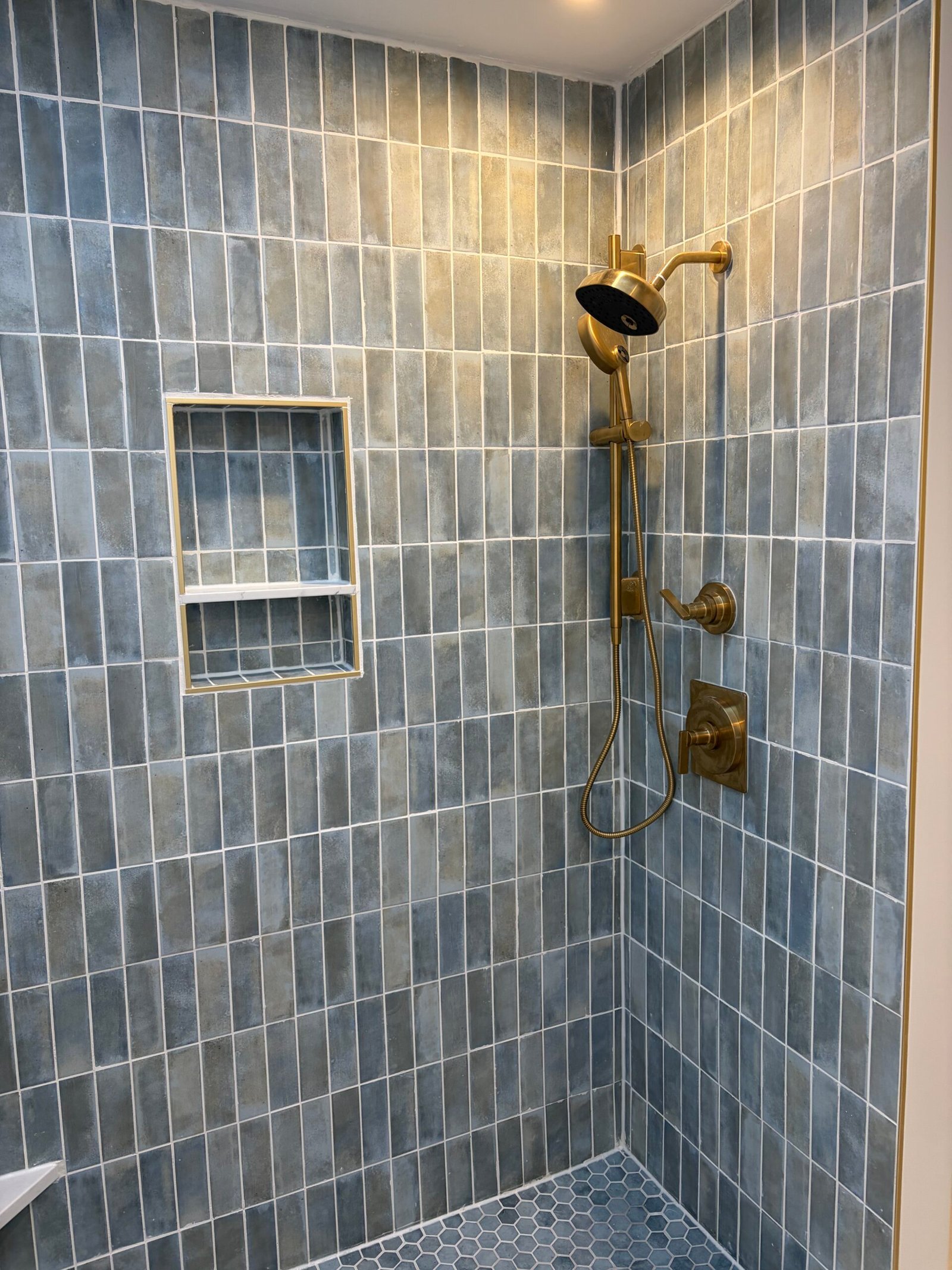 The showerhead, handheld shower and controls against the blue-gray tile.