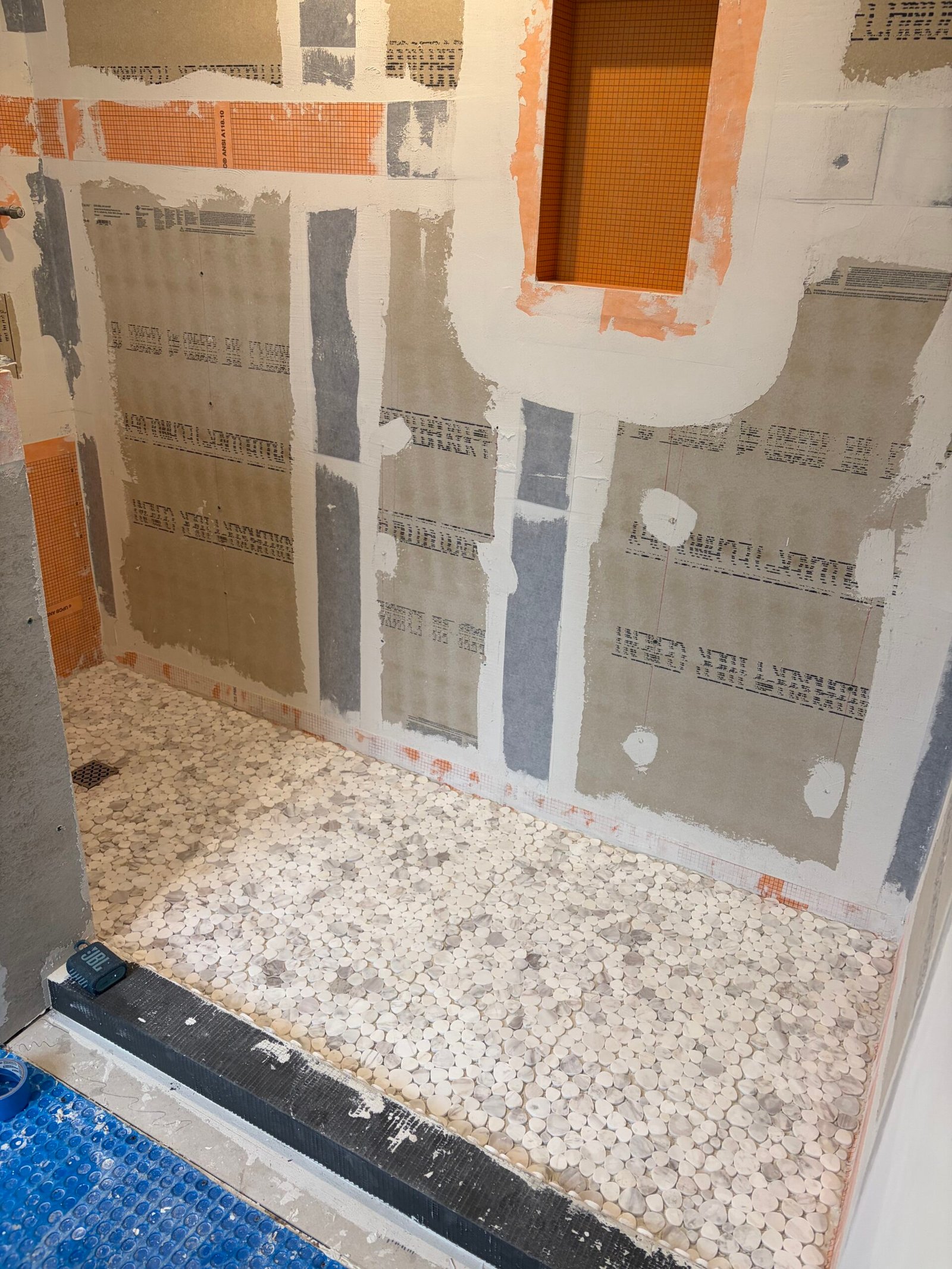 Mosaic shower-floor tile beside the prepared wall panels and niche.
