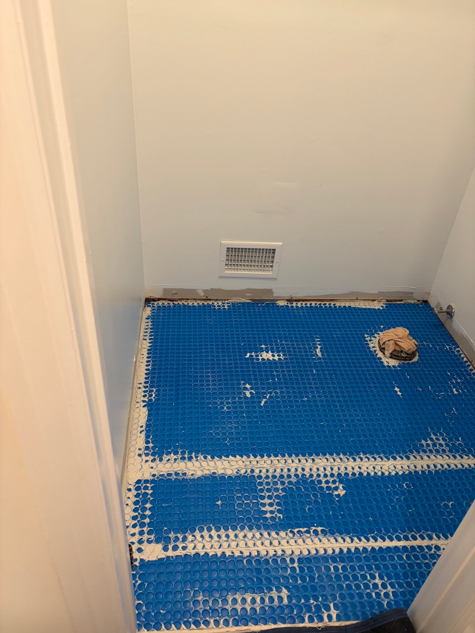Blue floor underlayment installed across the powder room, with the toilet drain left accessible.