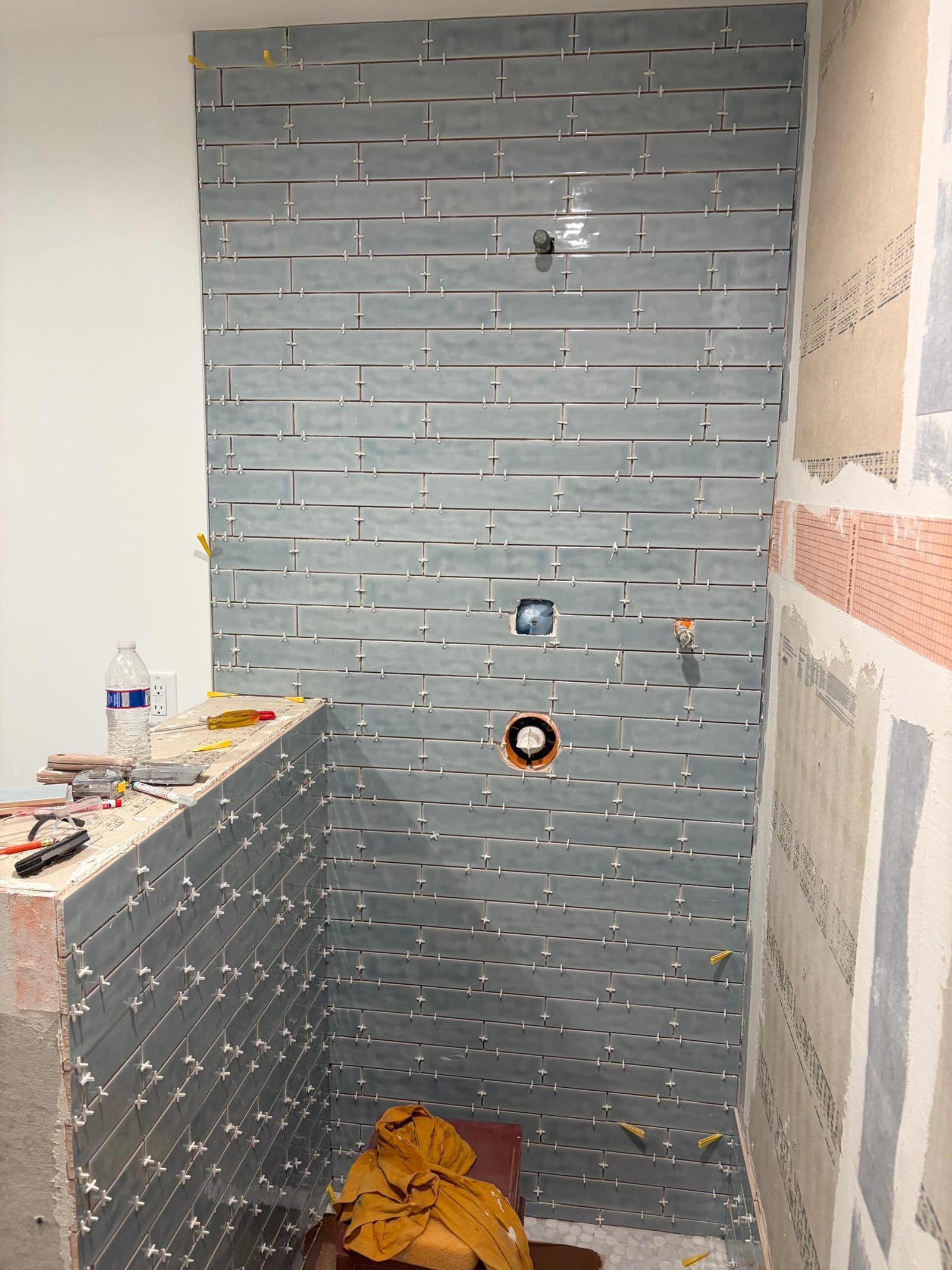 Blue subway-style wall tile being installed around the shower fittings.