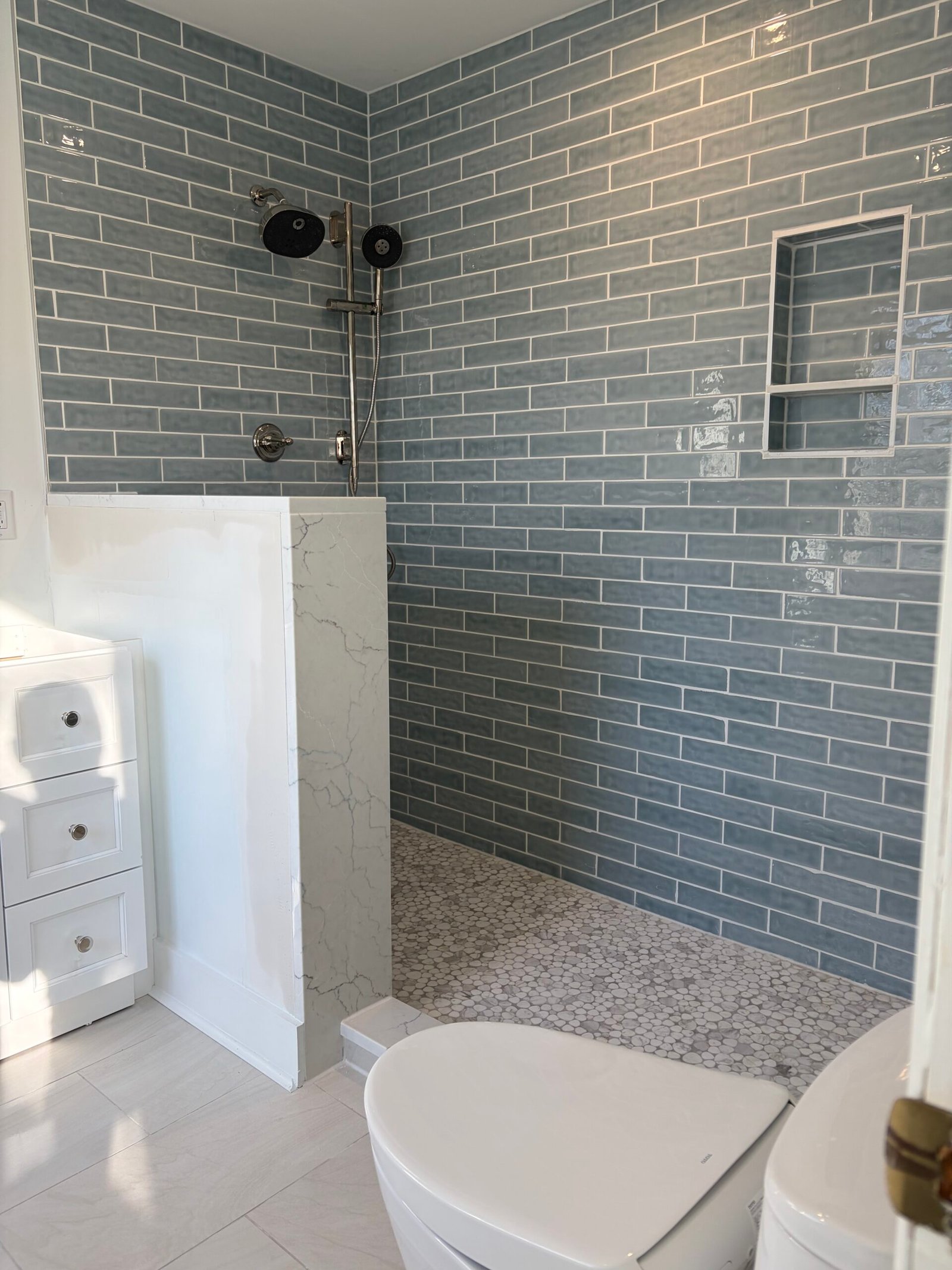 After: the blue-tiled walk-in shower, white partition, vanity and updated toilet.