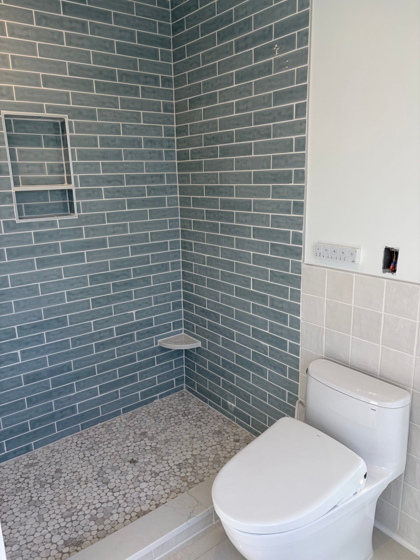 After: the walk-in shower and adjacent toilet, with the blue tile and light floor together.