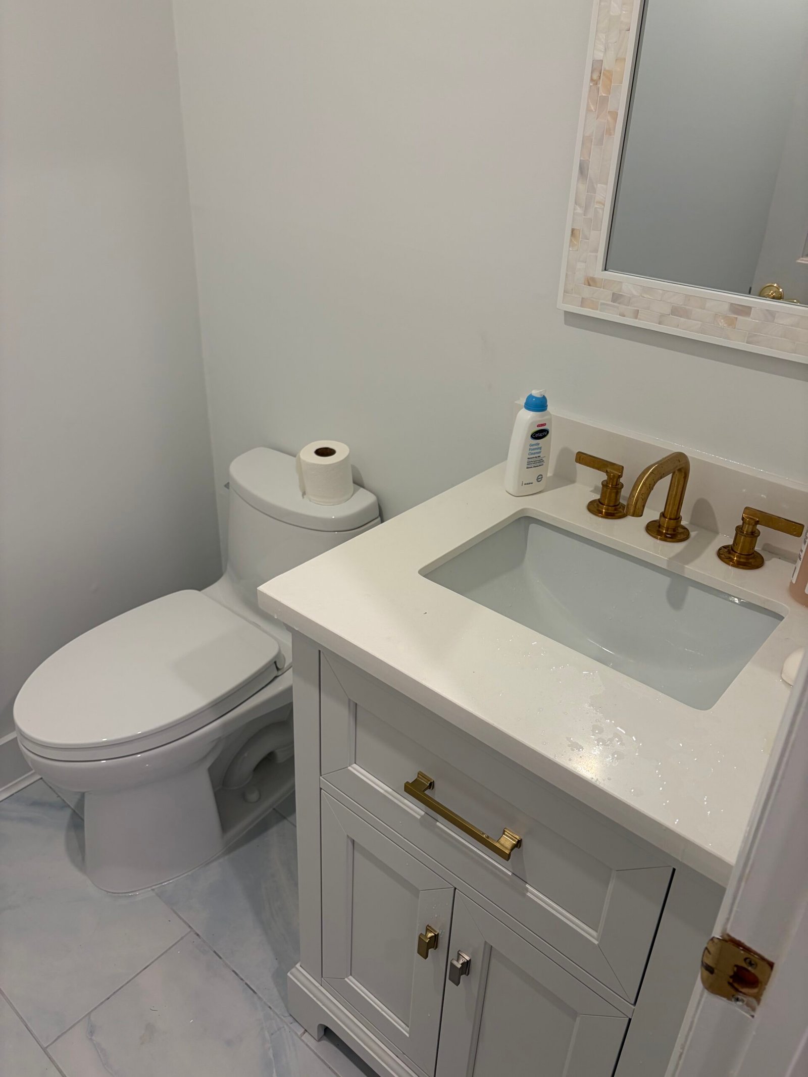 After: the toilet and gray vanity together, with matching brass-tone hardware and light floor tile.