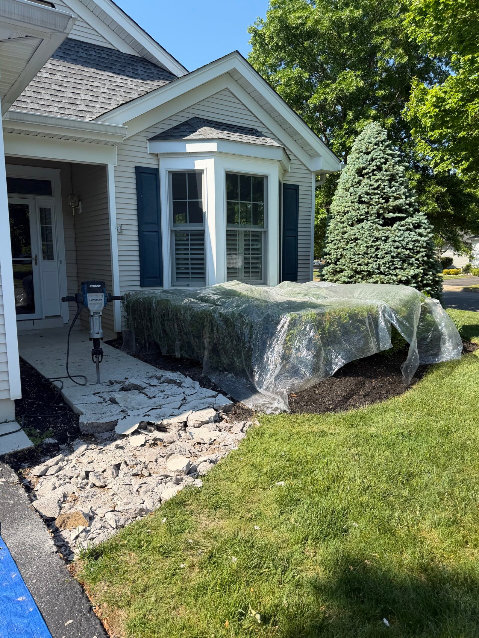 Concrete removal in progress, with the neighboring shrubs covered for protection.
