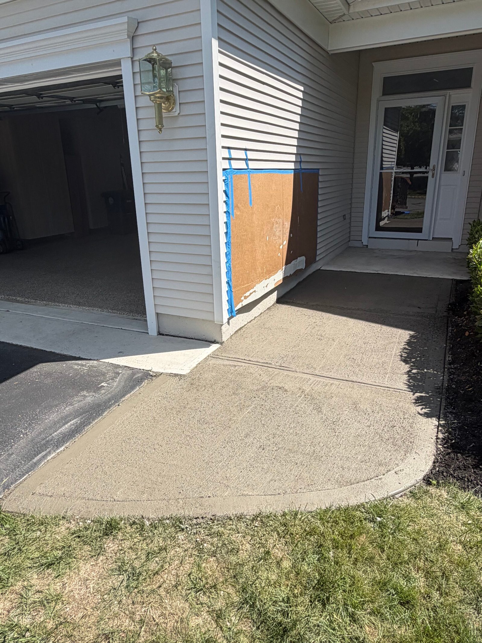Fresh replacement concrete at the garage corner, with the siding protected.