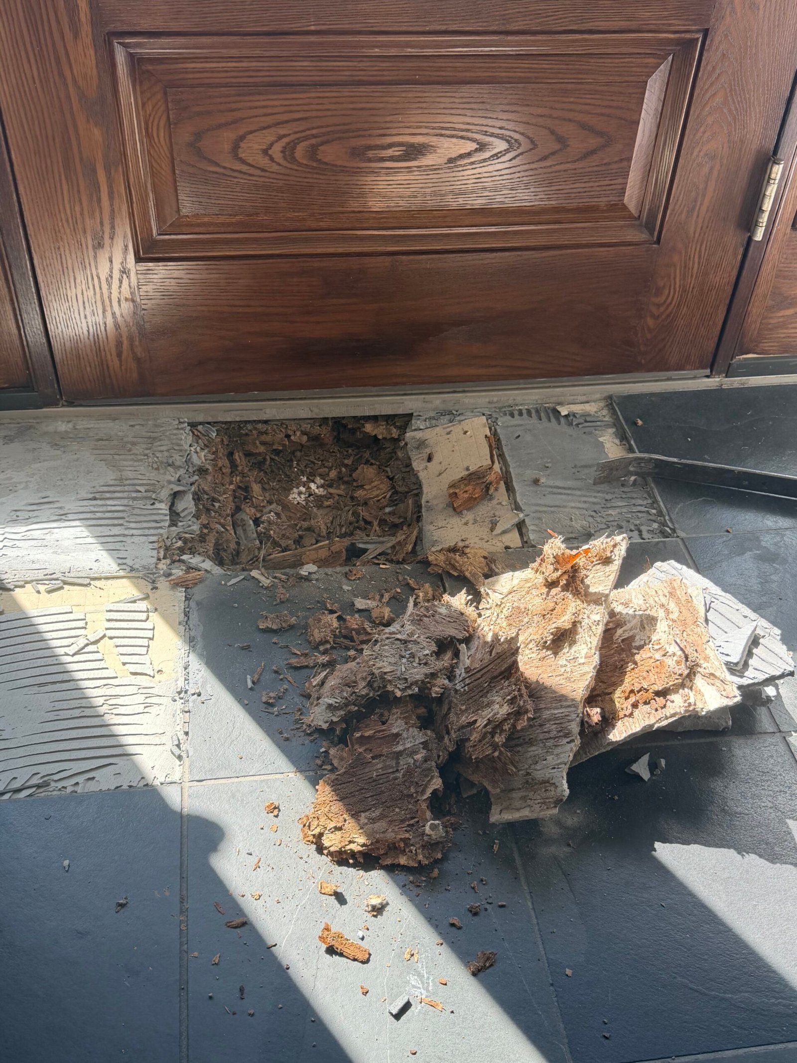 Initial tile removal exposing deteriorated material beneath the entry surface.