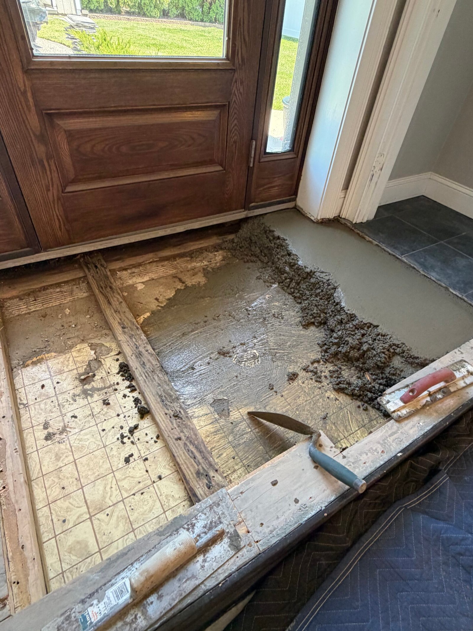 Gray base material being placed and worked across the opened entry floor.