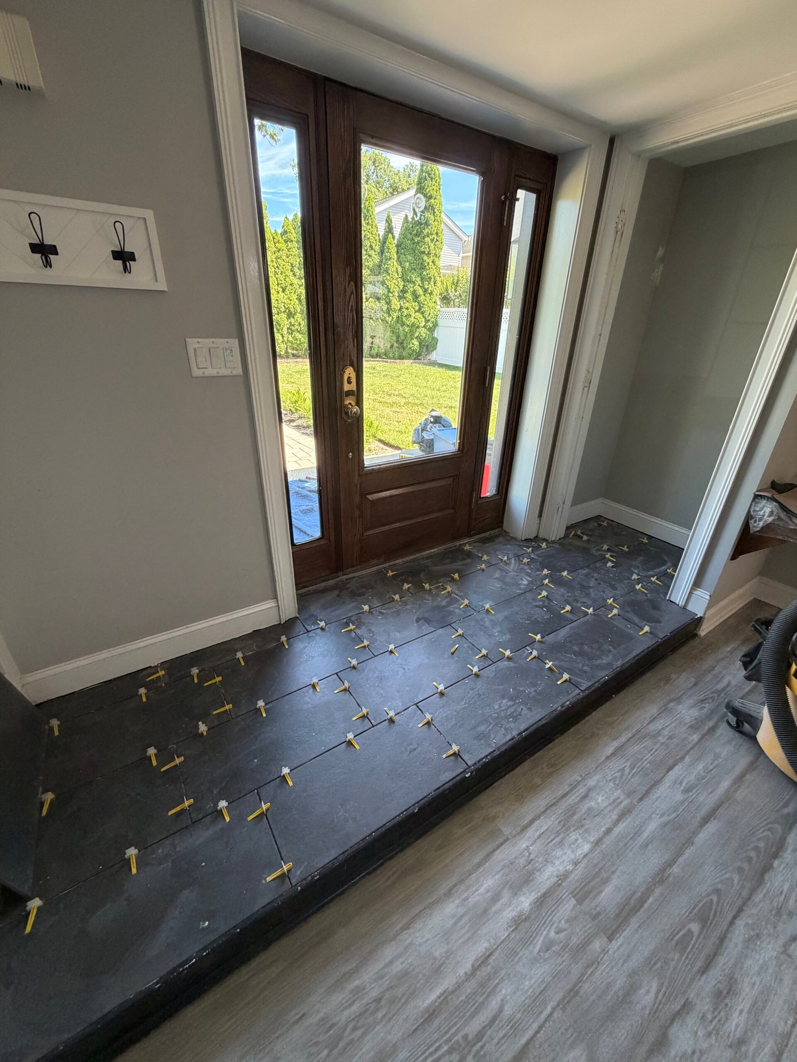 The tile installation advancing across the entry, with clips along the joints.