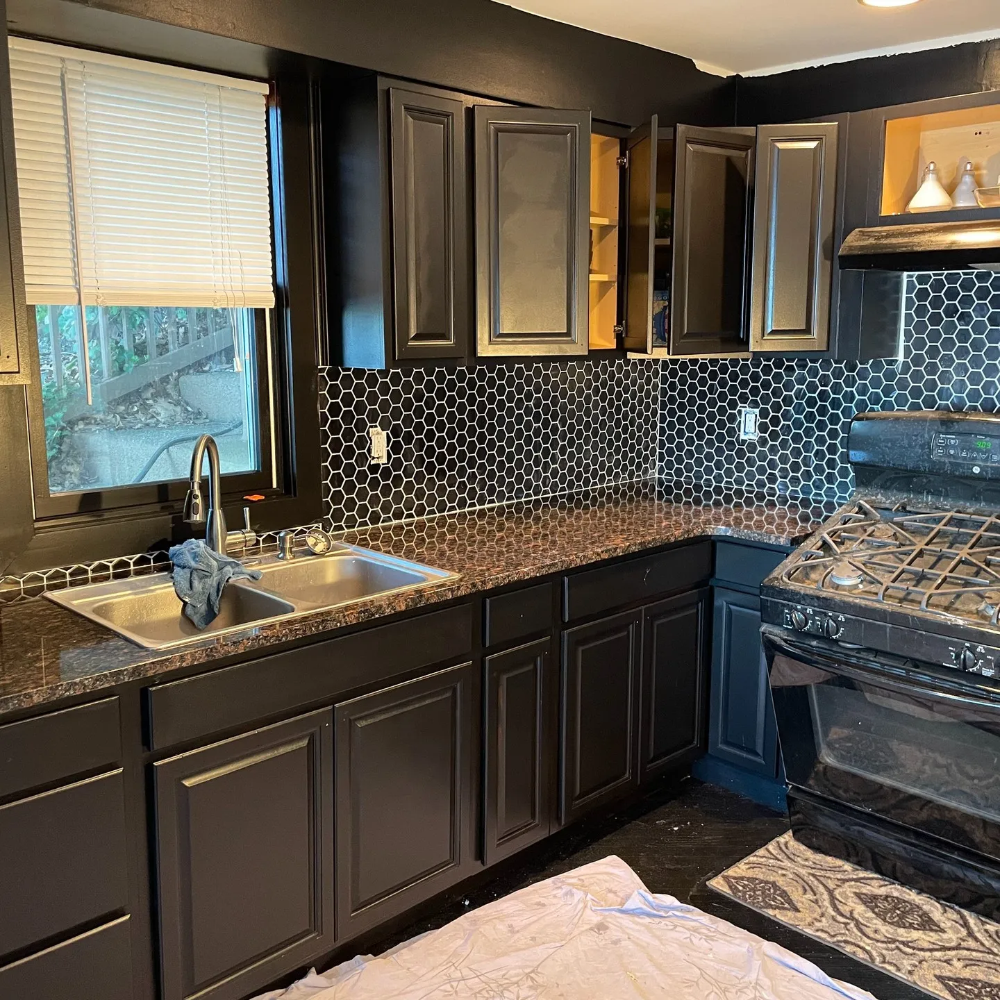 Later view: dark-painted cabinets and a black hexagonal backsplash along the sink, corner and cooking area.
