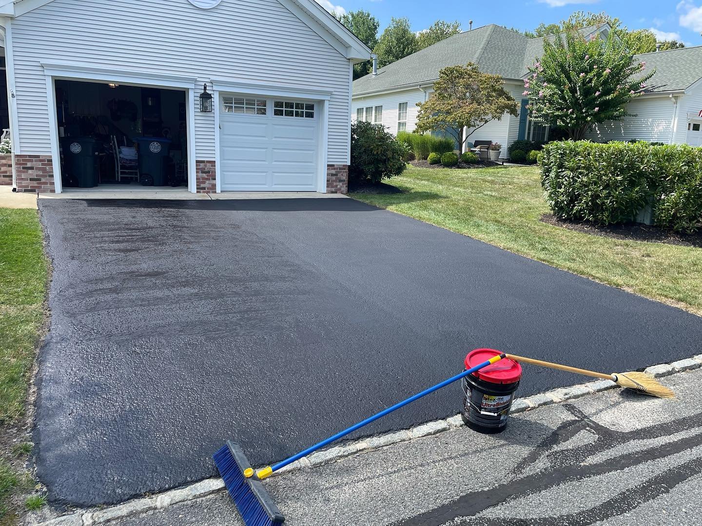 The renewed dark asphalt coating across the driveway, viewed toward the garage.