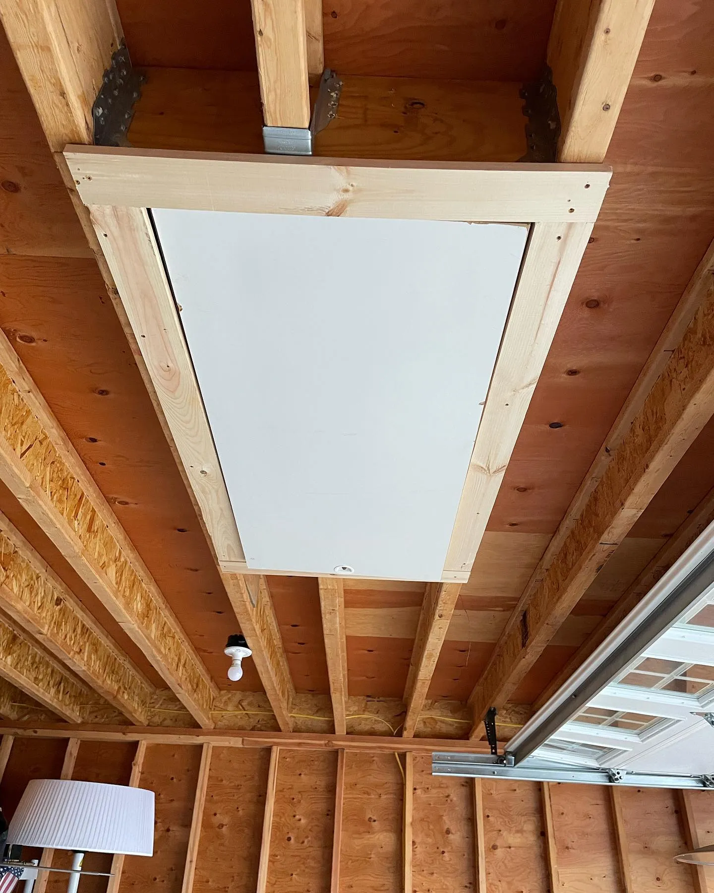 The closed white attic hatch, finished around the opening with wood trim.
