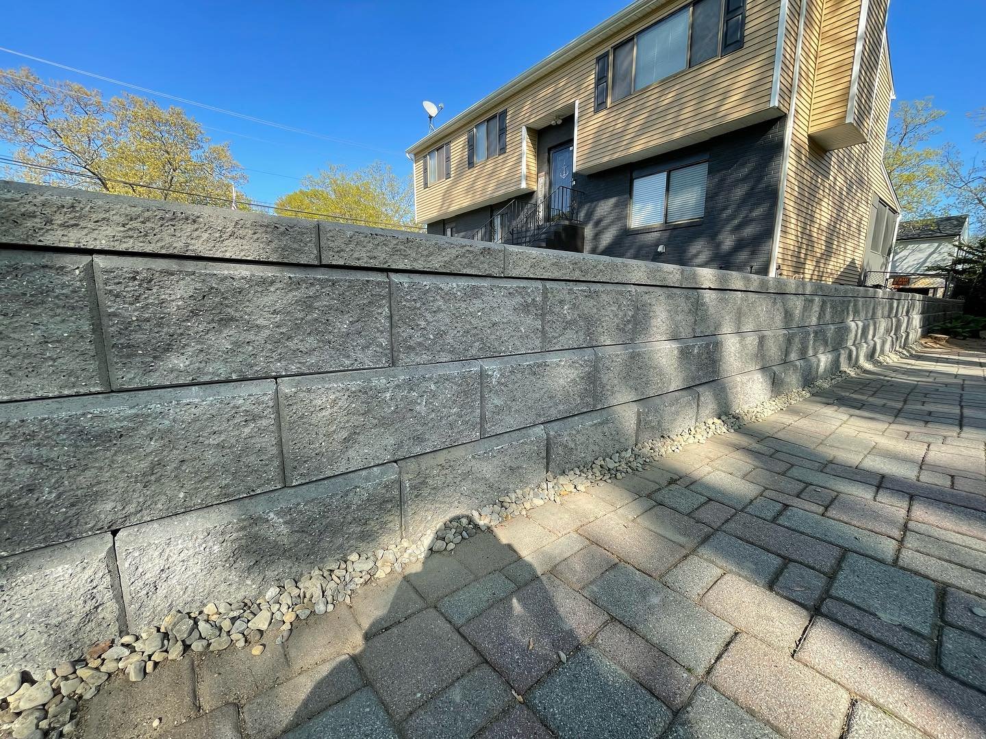 After: the rebuilt retaining wall with textured gray block faces, staggered joints and a continuous cap beside the pavers.