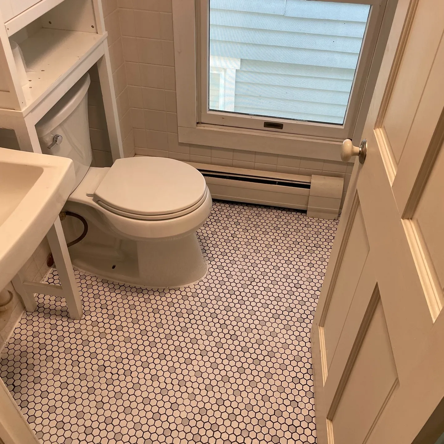 After the floor and toilet work: white hexagonal mosaic tile with dark joint lines and the toilet installed in place.