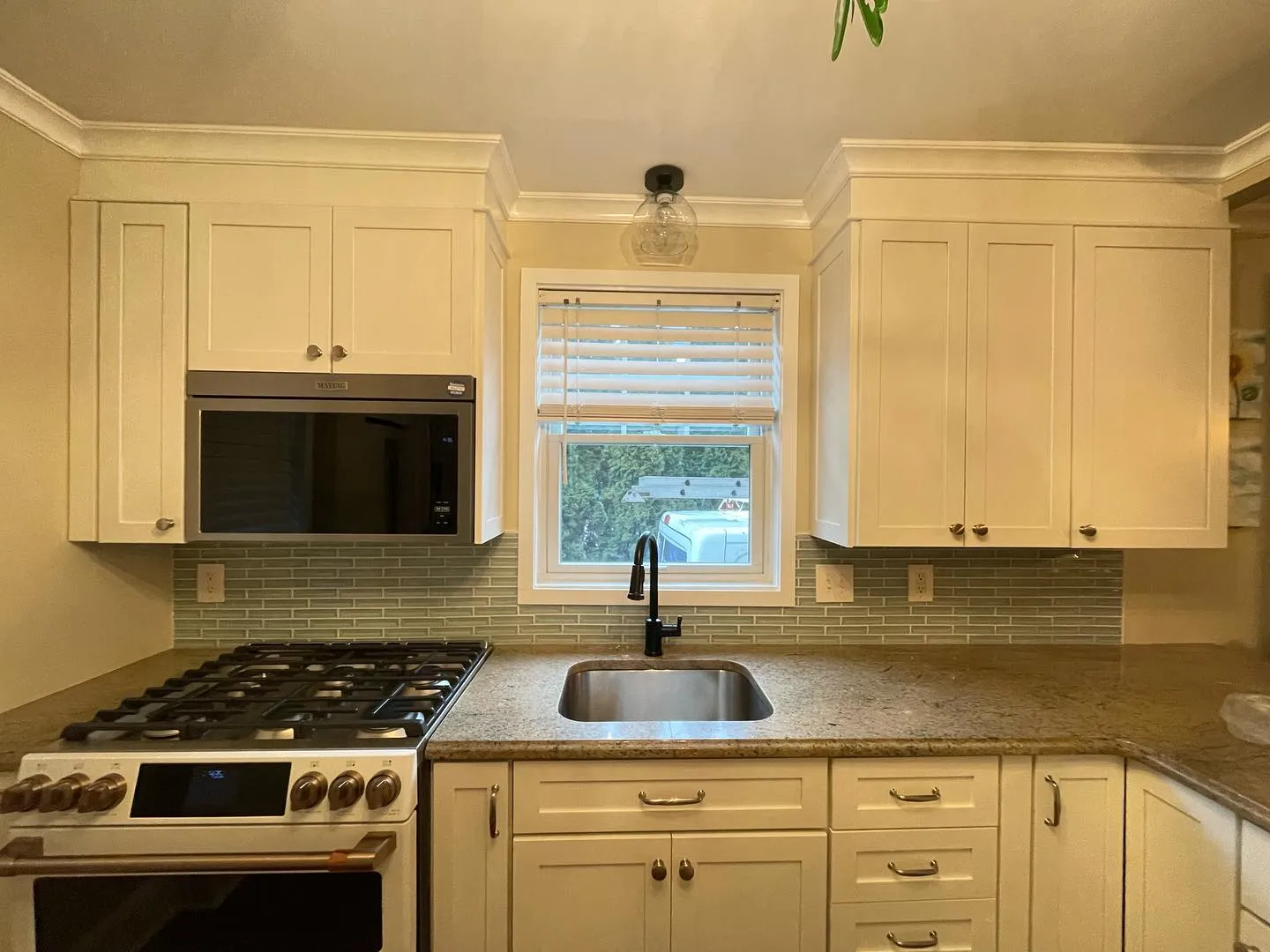 After: the renewed cabinet finish, crown molding, tile backsplash and replacement light at the window.