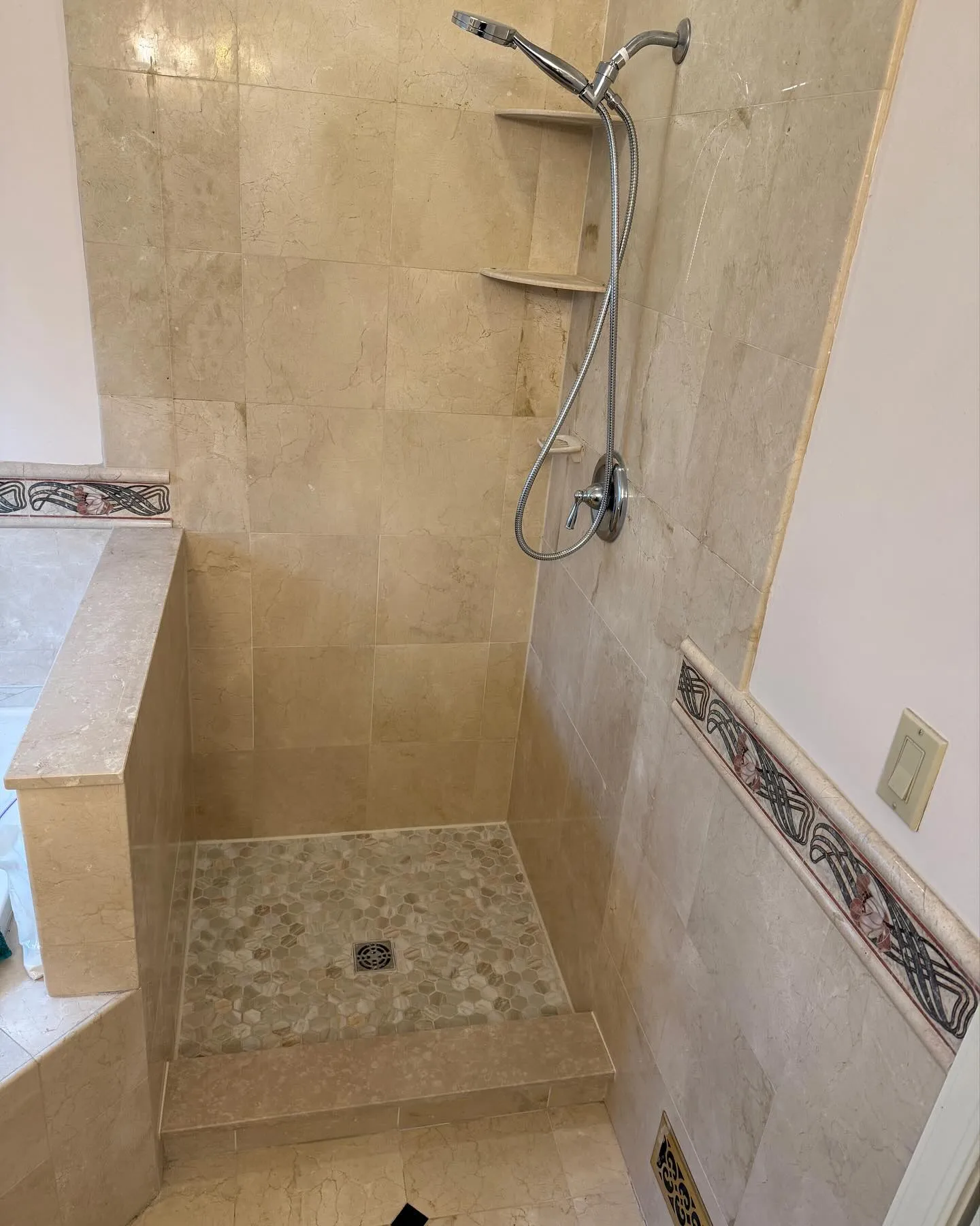After: the renovated shower base with light mosaic tile, a finished beige curb and the tiled walls above.
