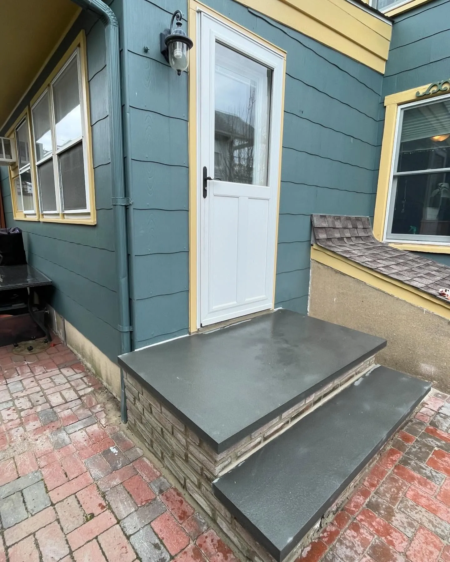 After: the finished dark landing and lower tread viewed from the side, showing the slab edges above the brick base.
