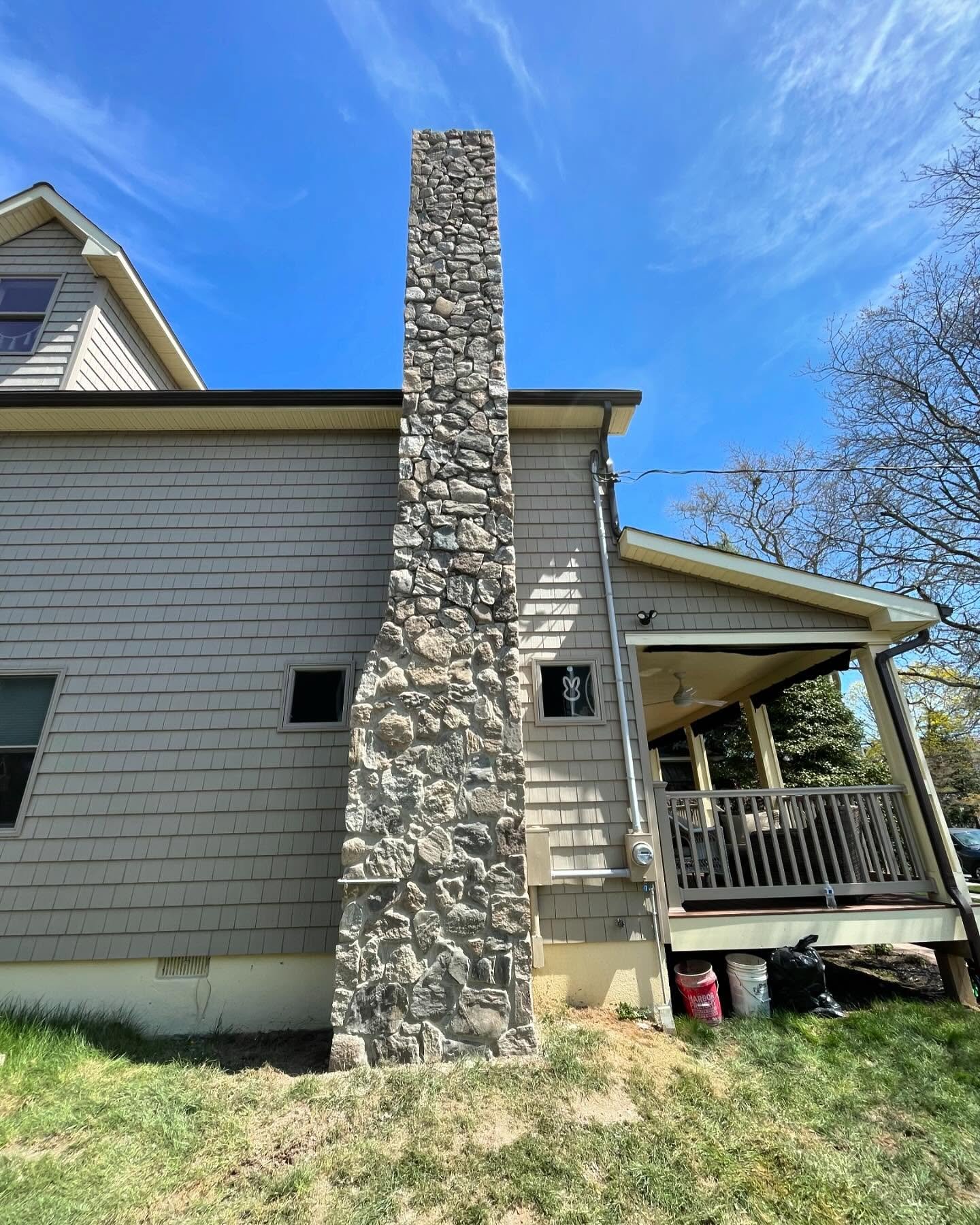 After: the completed gray stone chimney face, with irregular units and corner details continuing above the roofline.