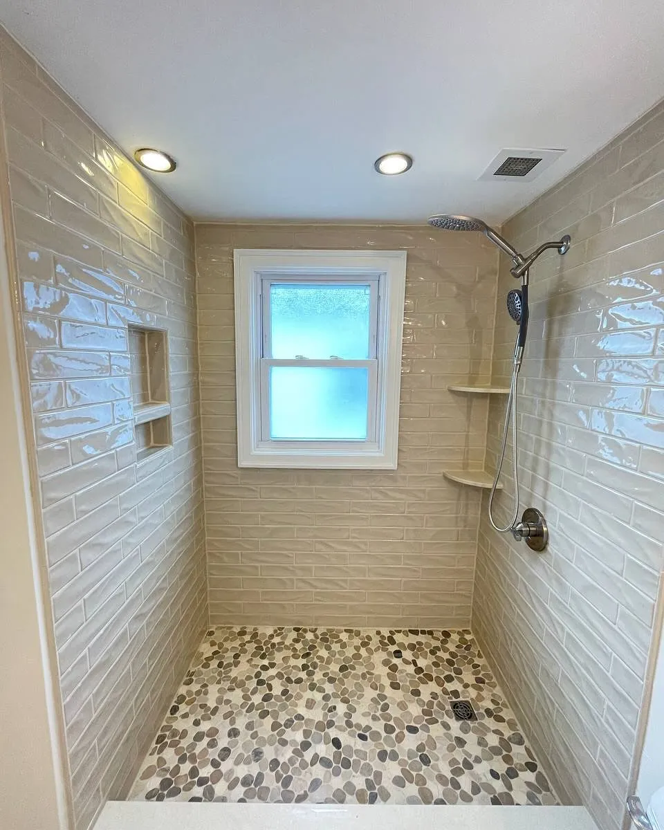 After: the shower with light textured wall tile, a multitone mosaic floor and white window trim.