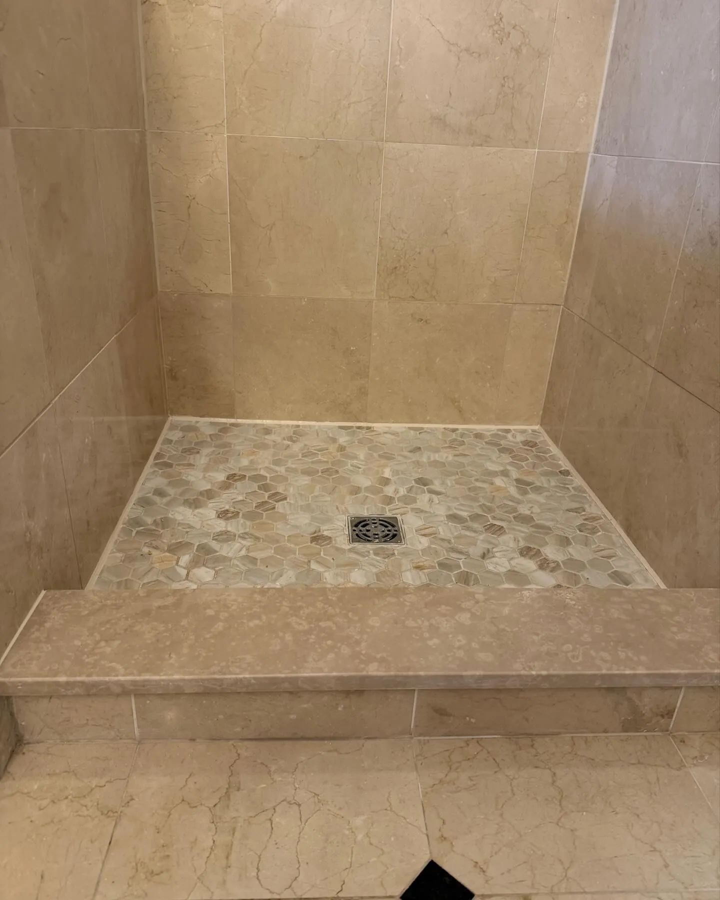 After: the light hexagonal mosaic shower floor, square drain grate and matching beige curb.
