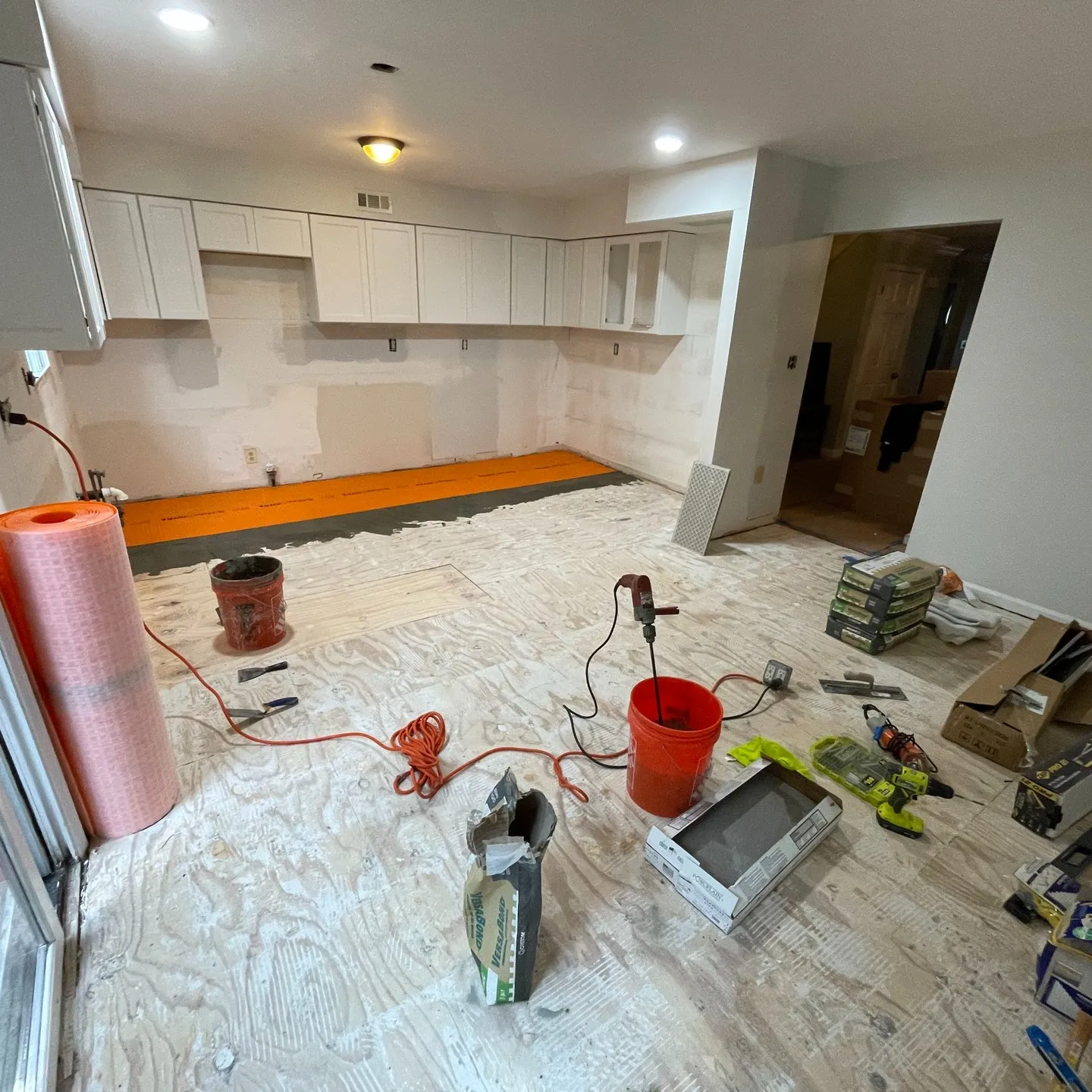 Floor preparation in progress, with exposed layers, mortar ridges and orange underlayment visible at the far wall.