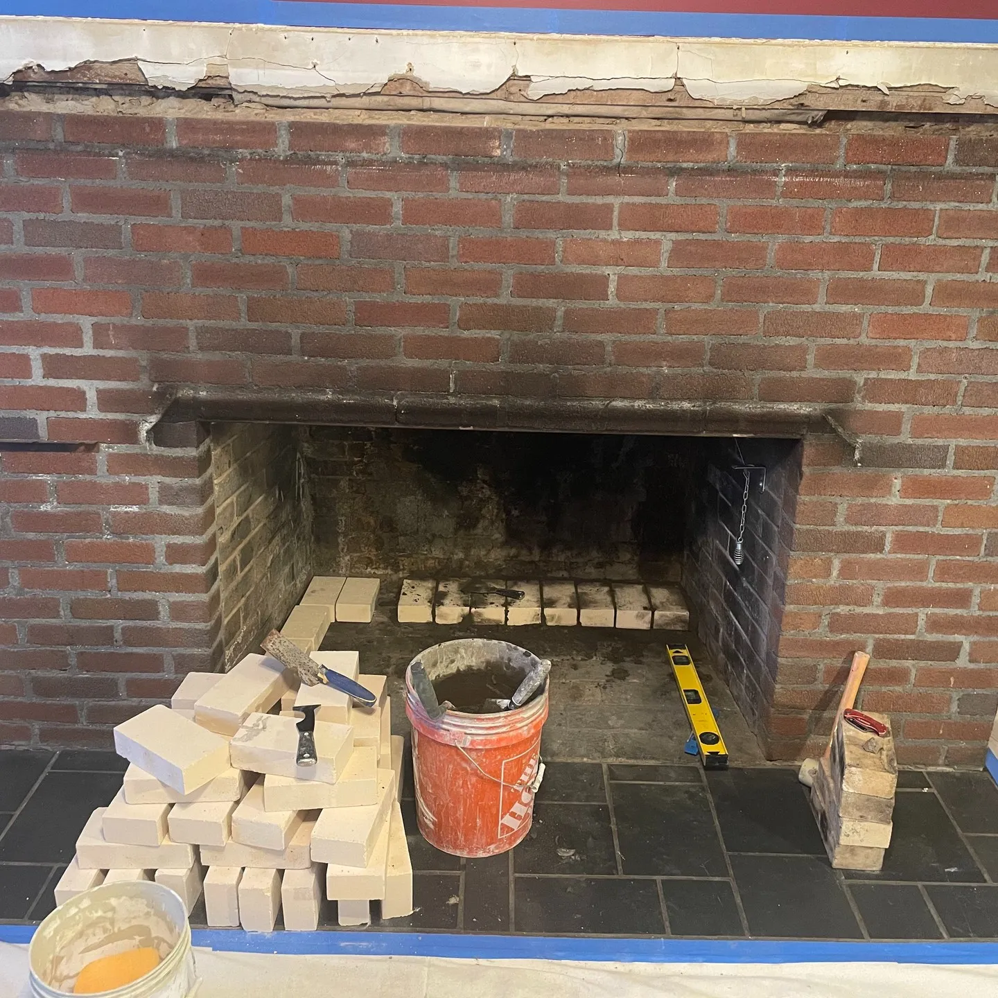 Early work stage: exposed brick facing, masonry units and tools at the fireplace opening.