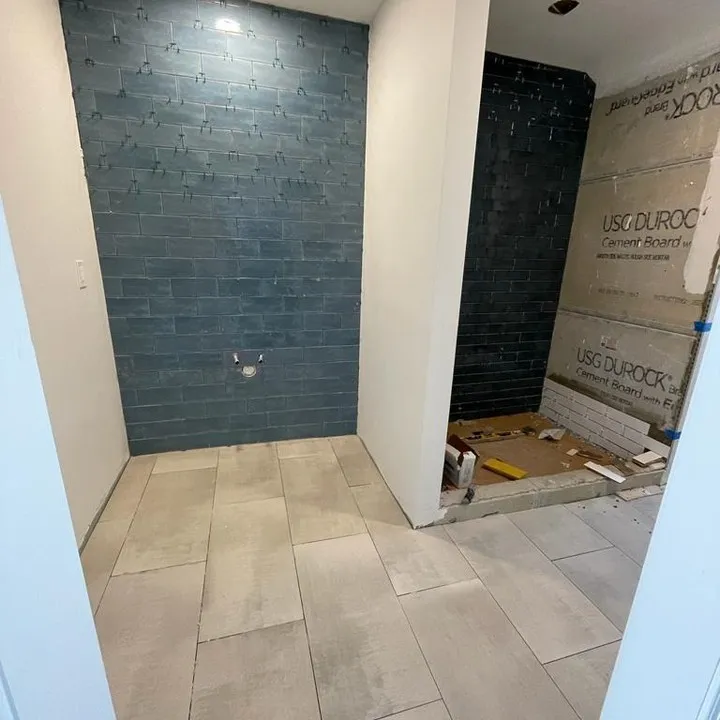 Blue wall tile at the future sink position, with spacers still in place and shower work continuing beside it.