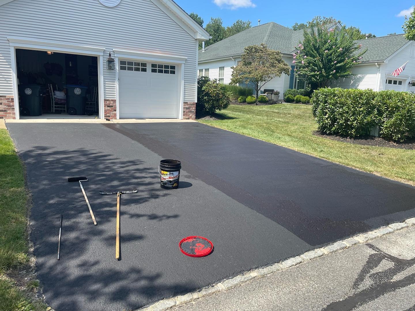 During application: contrasting coating bands across the existing asphalt driveway, with tools and a coating bucket in view.