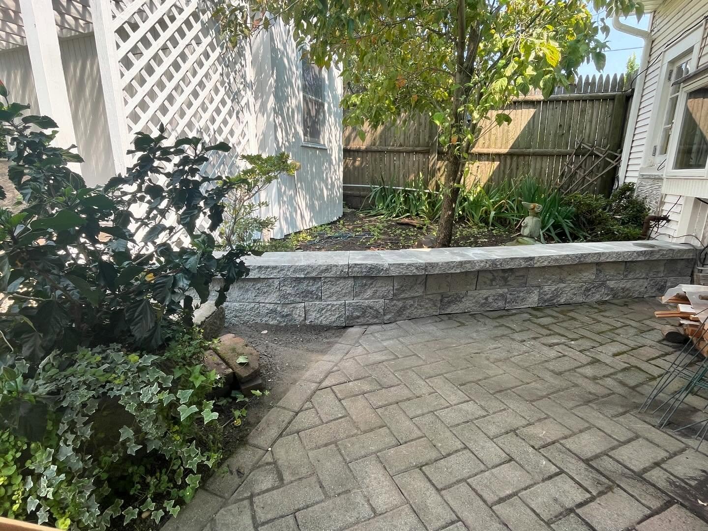 The finished garden border wall with textured gray blocks and Bluestone caps beside the paver path.