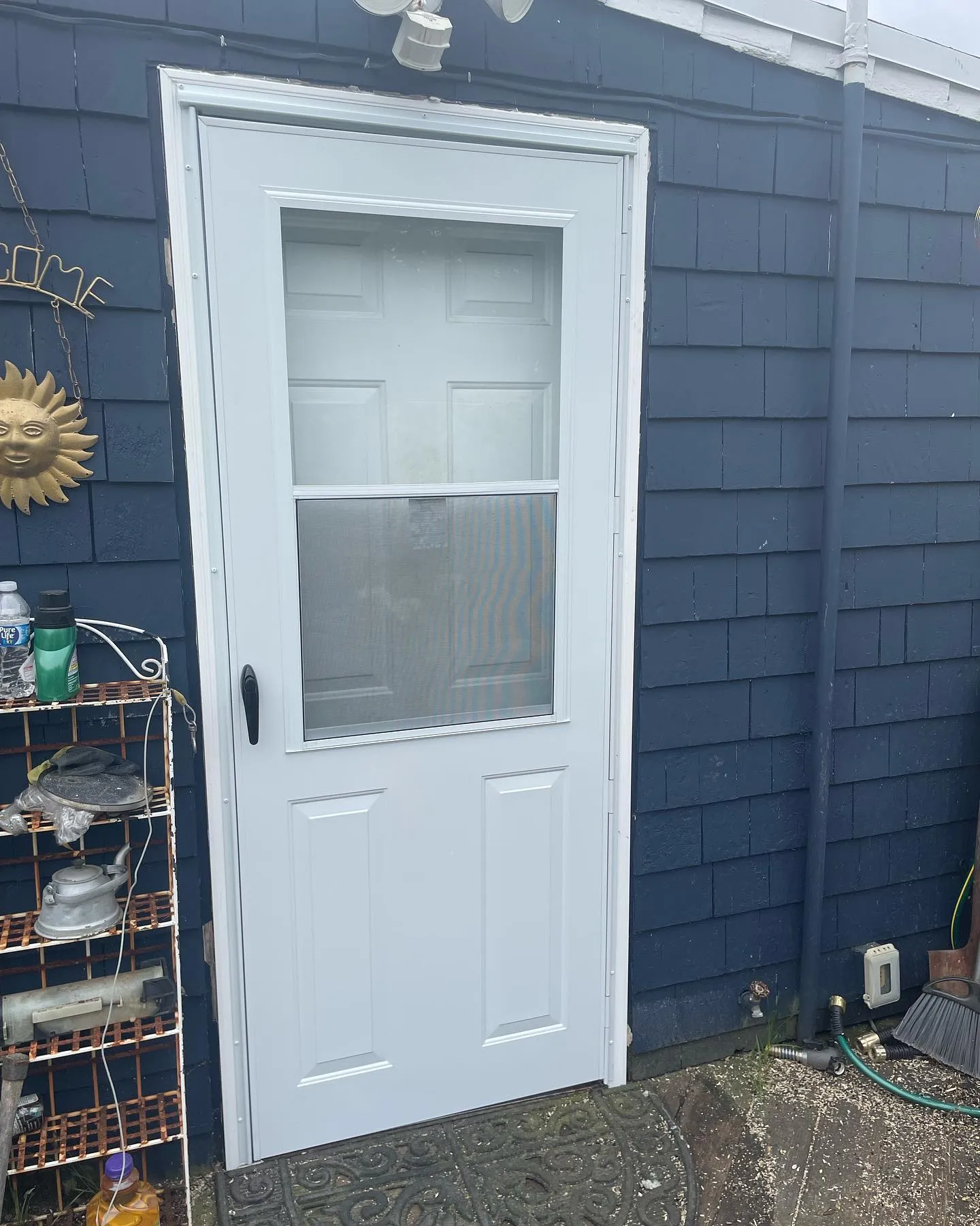 After: the replacement white storm door with a black handle at the blue-sided entrance.