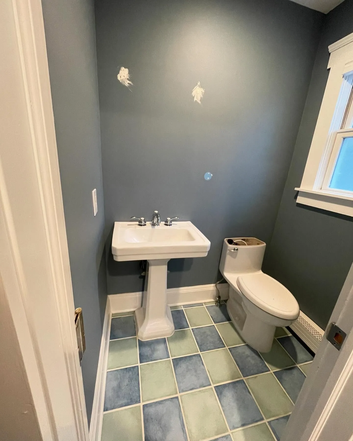 Before: the pedestal sink, existing toilet and blue-green square floor tiles, with marks on the wall above the sink.